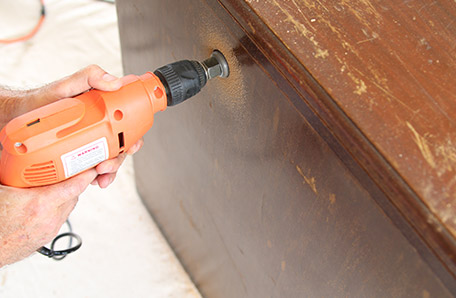 Using an electric drill with a keyhole bit to drill a hole for electric cords