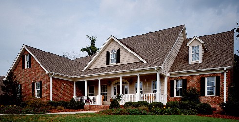 Ranch themed house with light brown walls, red brick, white trim and black shutters.