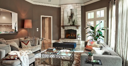 Bold global styled living room with brown on walls, white on trim, light gray couches, and a stone fireplace