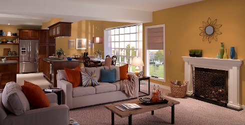 Open concept living room with dark mustard on walls, white on trim and fireplace and light taupe couch and chair