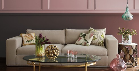 Shabby chic styled living room with mauve pink on top half of walls, magenta on bottom half, light beige couch, and floral throw pillows