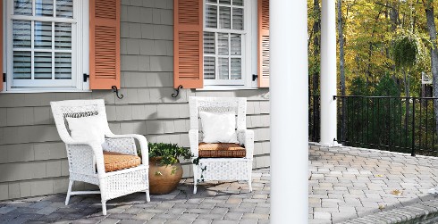 Two white wicker chairs on a stone front proch.
