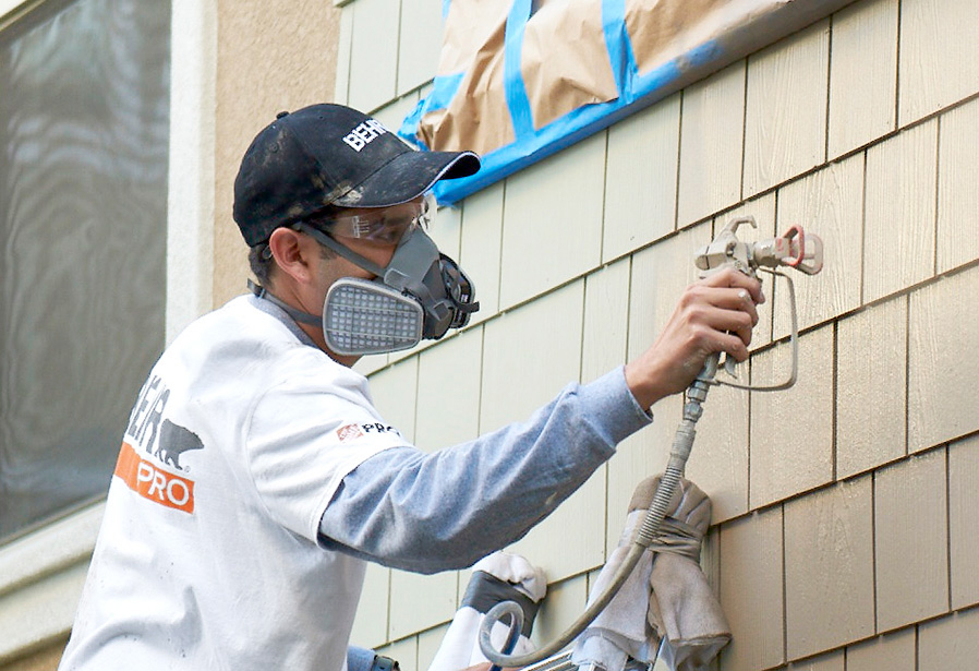 Pro Contractor wearing a cap and shirt with Behr logo dipping a paint brush on a 1 gallon of BEHR PRO e600 paint can on a porch that he is going to paint.