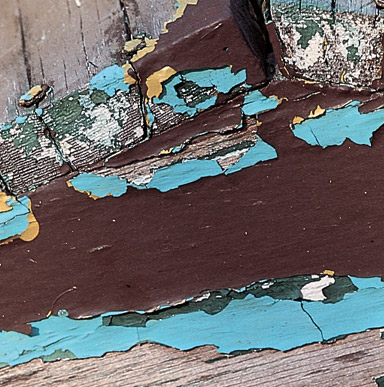 Close up image of a wood with peeling paint and underneath is another coat of a different colour.