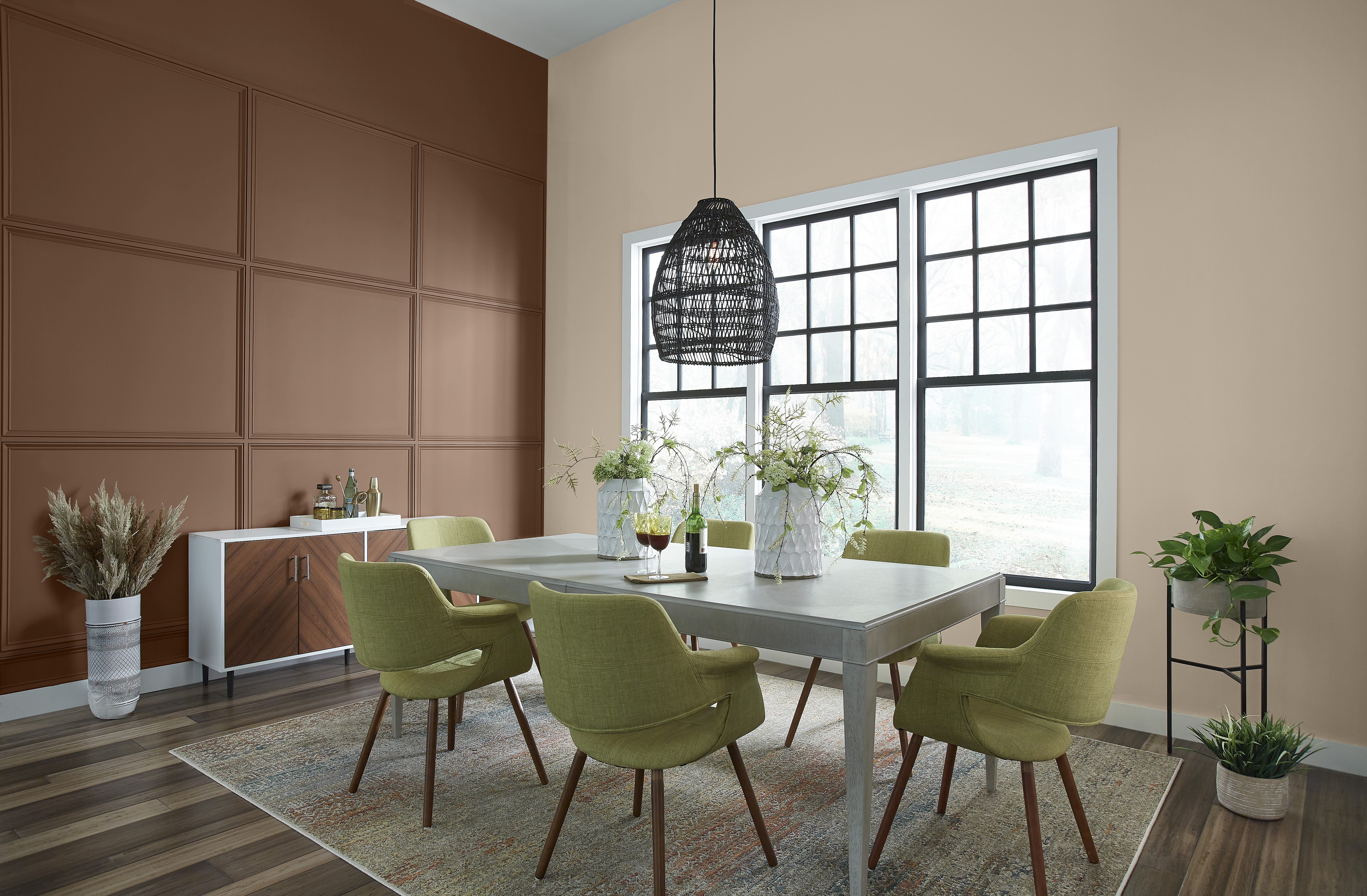 Une salle à manger éclectique avec une table moderne et des chaises rembourrées vertes. Un mur d'accent est peint avec une couleur brune appelée Mustang sauvage.
