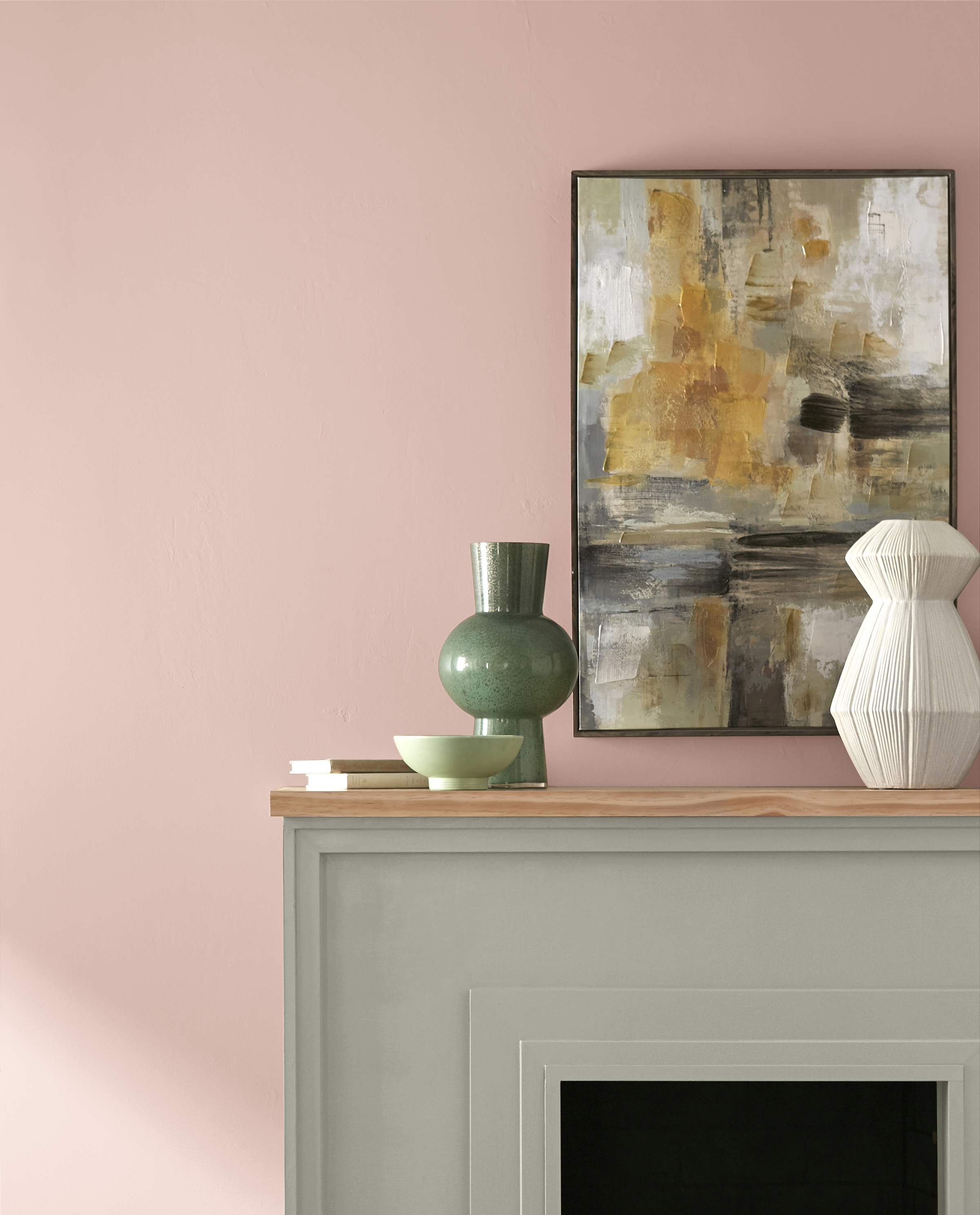 Une photo en gros plan d'un mur de salon avec foyer, le mur est peint en rose pâle et le manteau de cheminée est peint en un gris-vert.