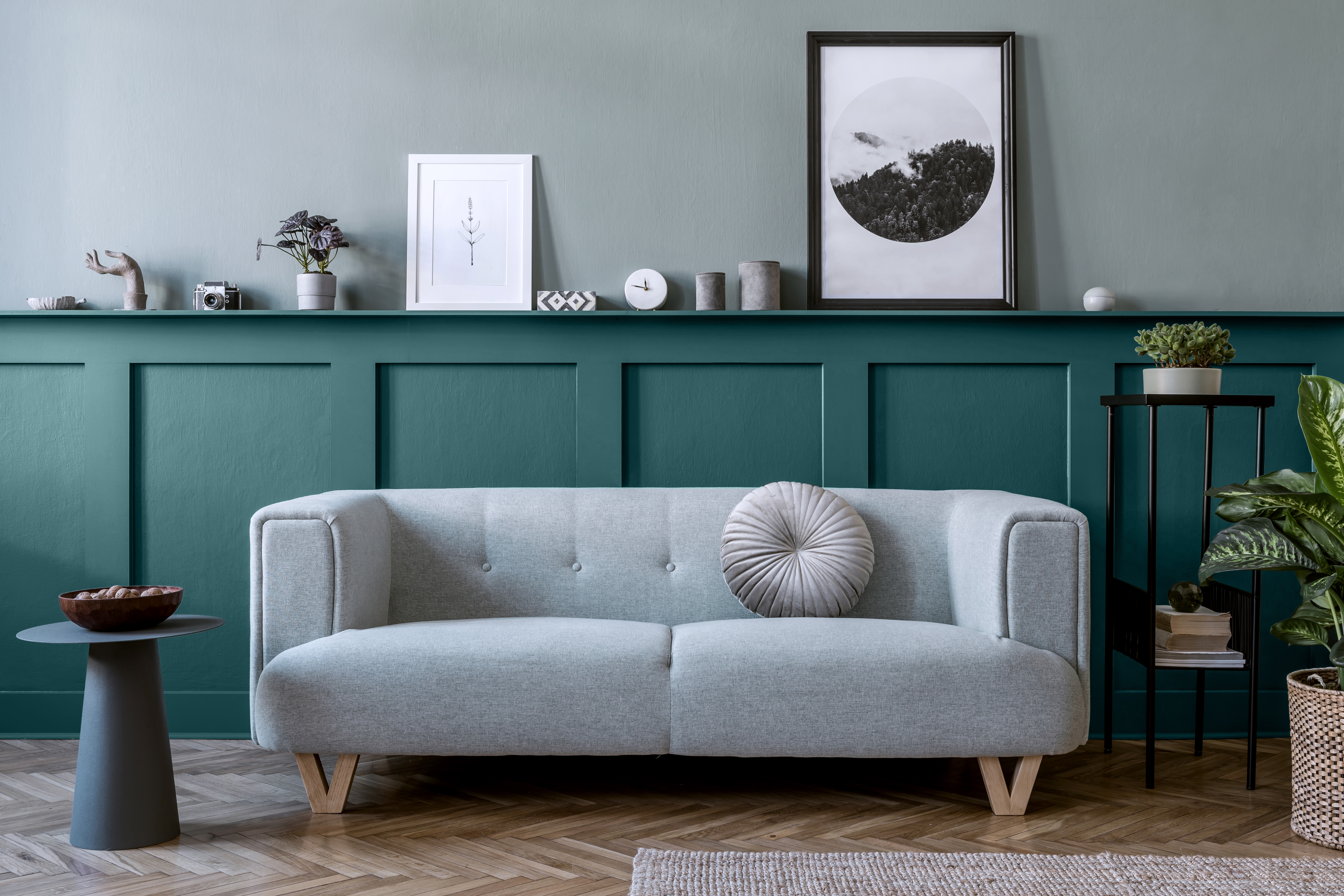 Un salon avec un mur d'accent inférieur. Le haut du mur est peint dans une couleur bleu-vert presque neutre appelée Aqueux. La couleur du mur inférieur s'appelle Abîme d'océan. La pièce est enjolivée d'éléments décoratifs décontractés et neutres comme le sofa rembourré gris clair, la table d'appoint noire et les petis objets décoratifs de couleur gris béton.