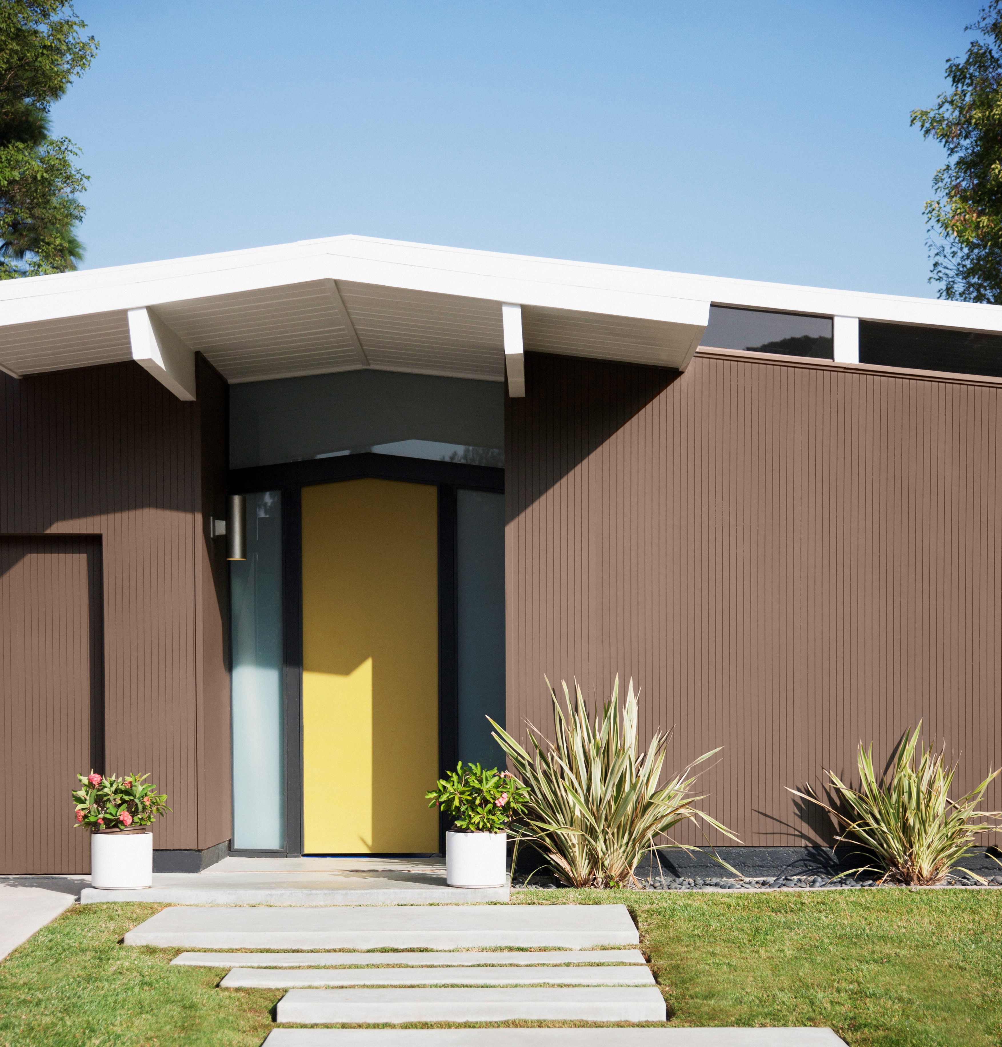 Une maison des années '50 dont le corps de la maison est peinturé en un brun stabilisant appelé Mustang sauvage. La porte d'entrée est peinte dans une couleur jaune vive et gaie. Aménagement paysager bien entretenu.