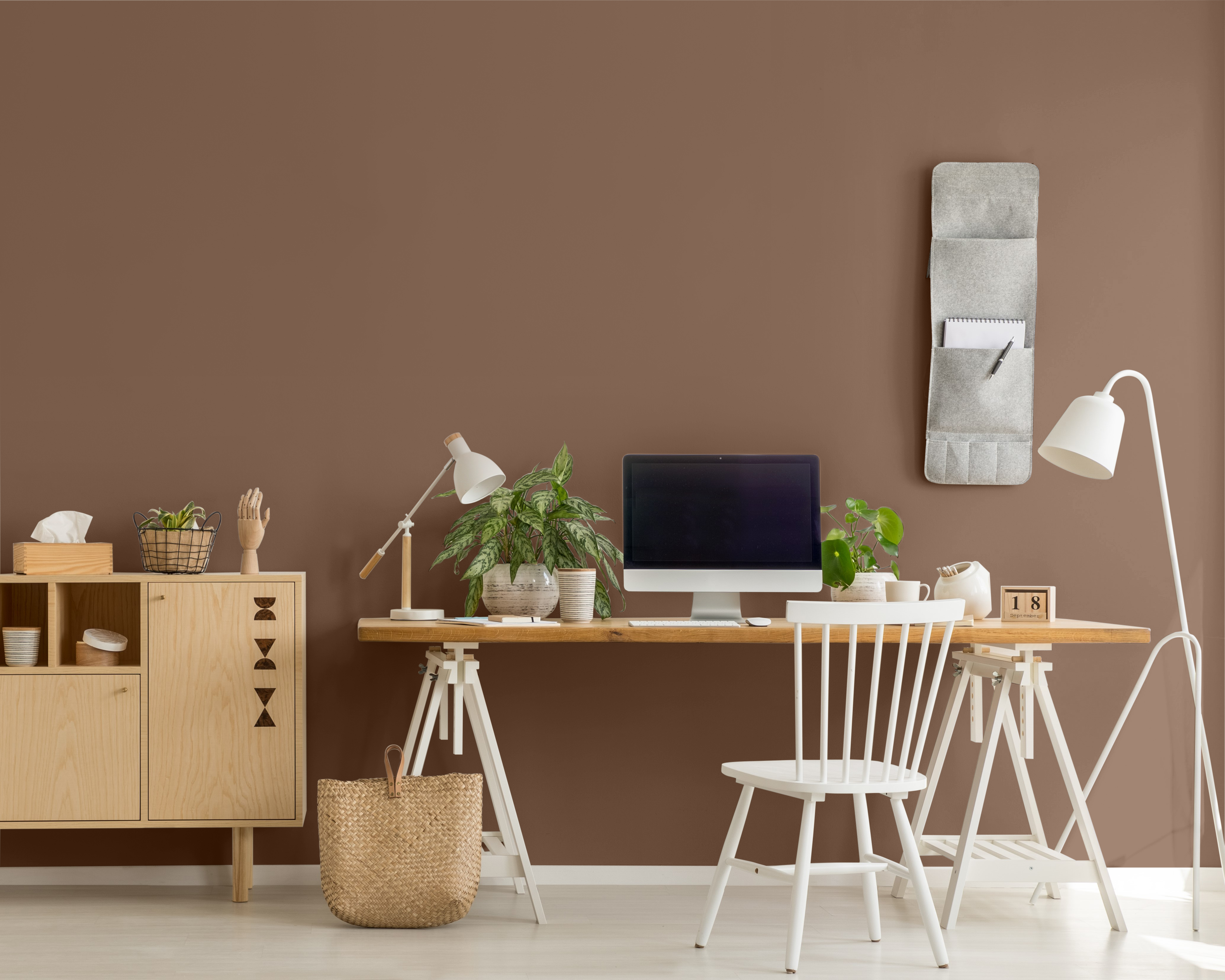 Une photo d'une petite armoire en bois à côté d'un pupitre sur lequel sont placés un ordinateur et des plantes dans un bureau à domicile. Le mur est peinturé en un brun appelé Mustang sauvage.