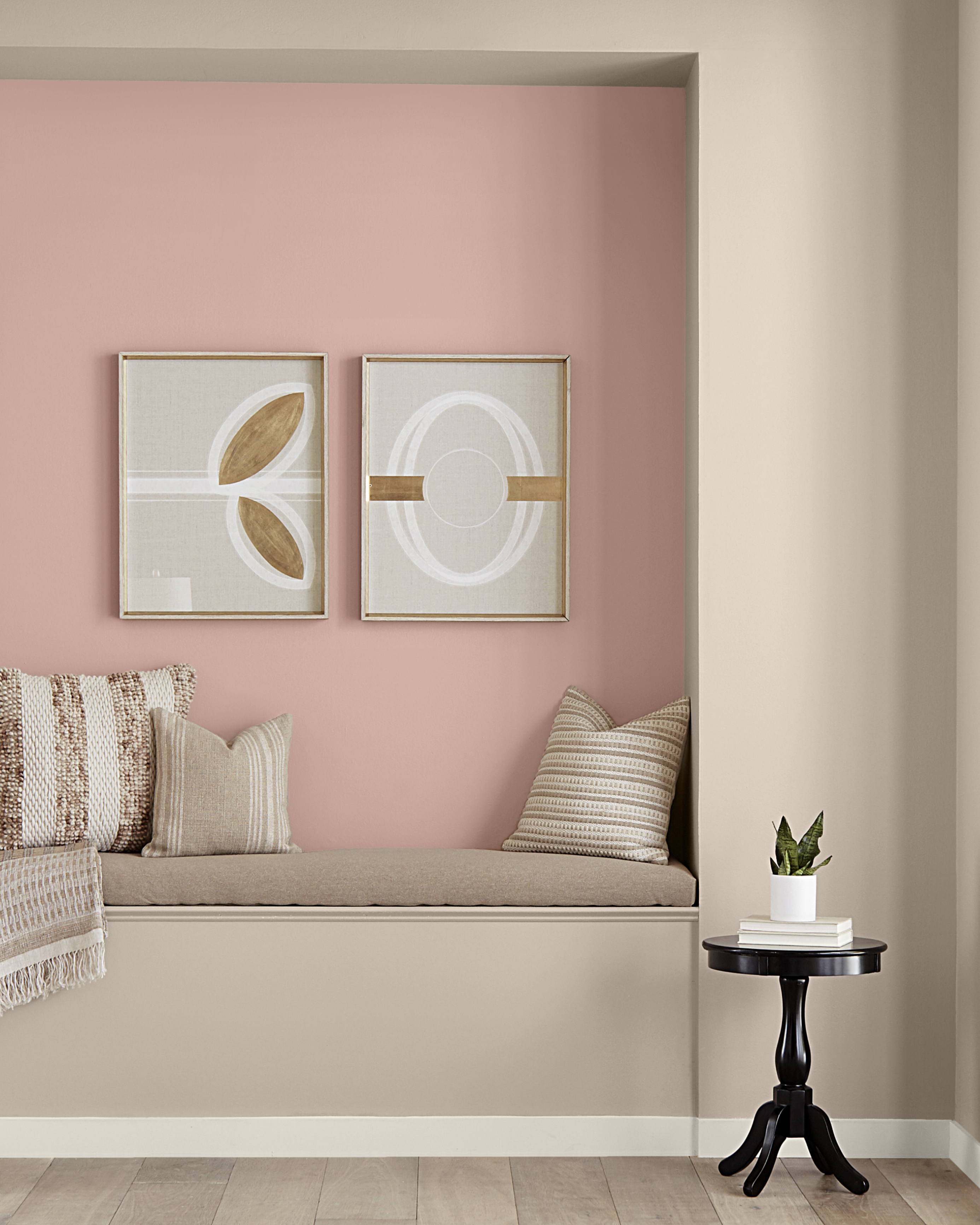 Un coin lecture dans le couloir avec mur de teinte rosée. Le mur d'accent est muni de deux affiches décoratives. La banquette présente des tons neutres.
