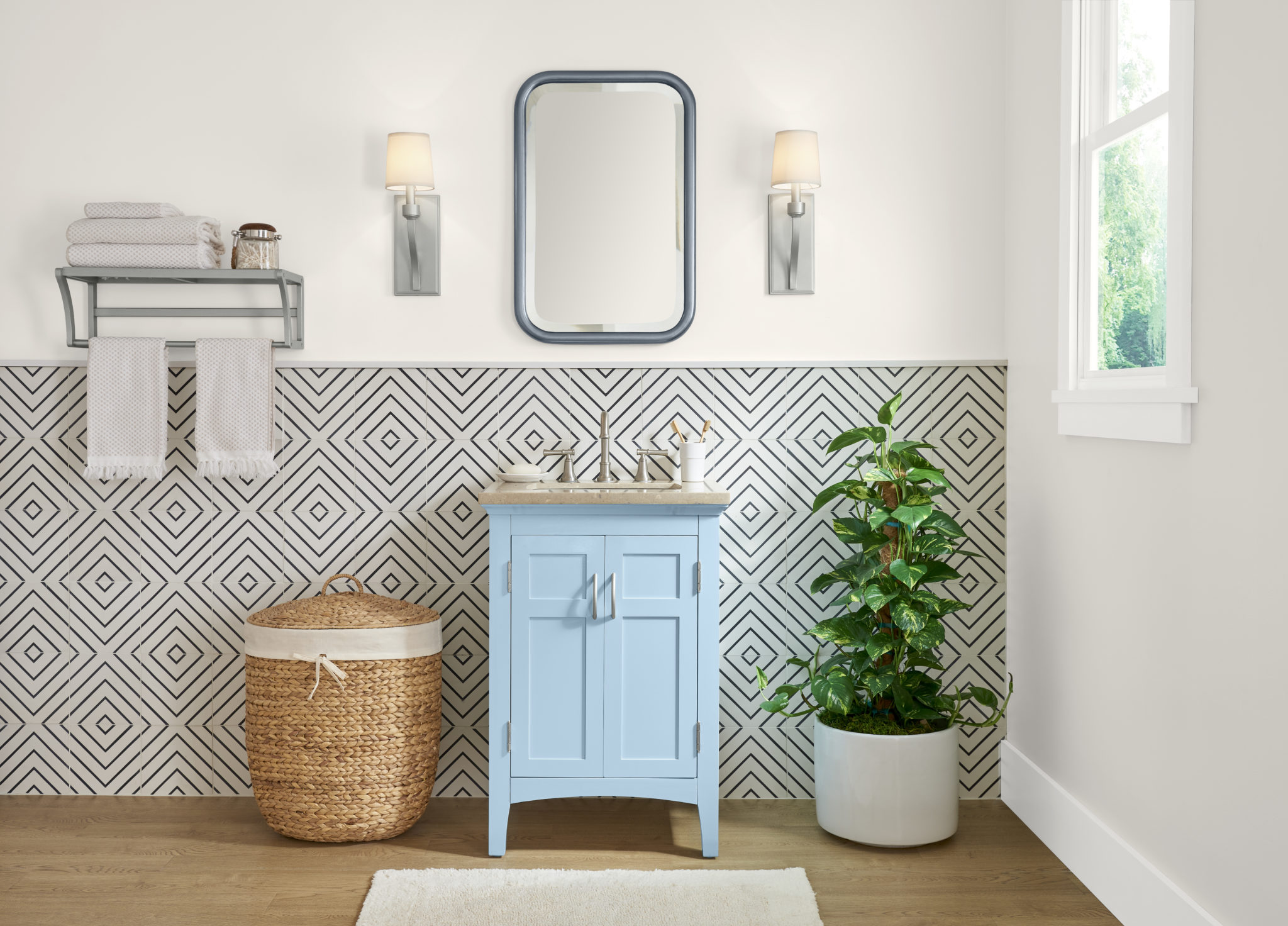 Une salle de bain avec un petit meuble-lavabo peinturé en bleu clair. Le mur d'accent inférieur est carrelé avec un motif géométrique noir et blanc.