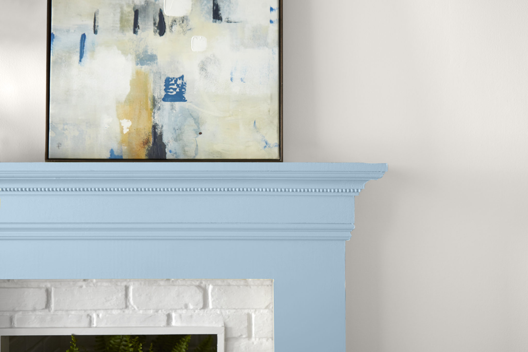 Un mur blanc avec un manteau de cheminée peint en bleu clair appelé Après la pluie. L'art mural abstrait complète le look.