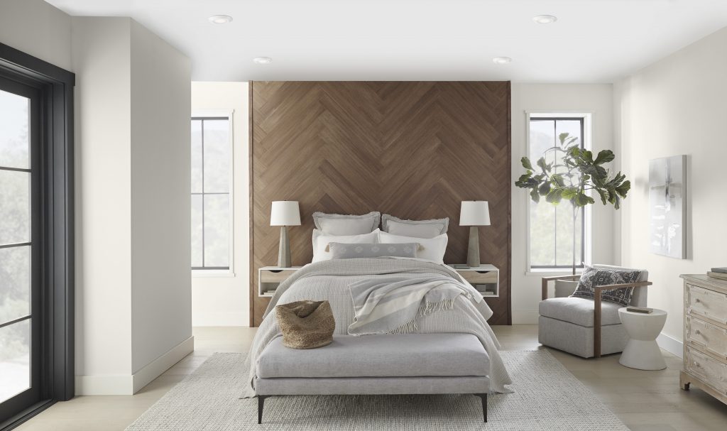 Une chambre à coucher élégante peinte dans un blanc serein et équilibré. Les teintes douces utilisées dans l'espace contrastent joliment avec le mur en bois.