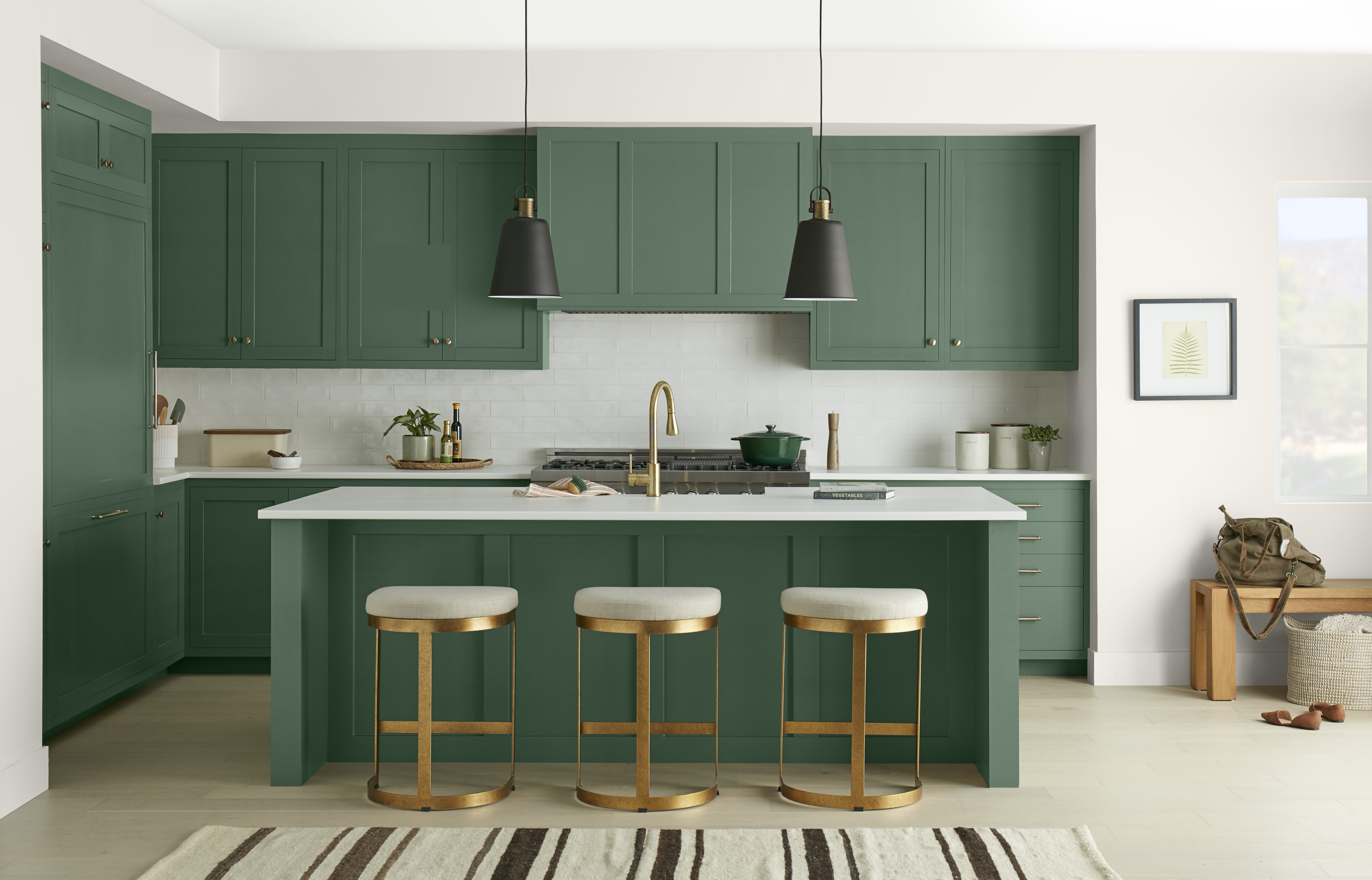 Une cuisine avec des armoires et un îlot peints dans une couleur de vert profond, stylisée avec des finitions modernes noires et dorées.