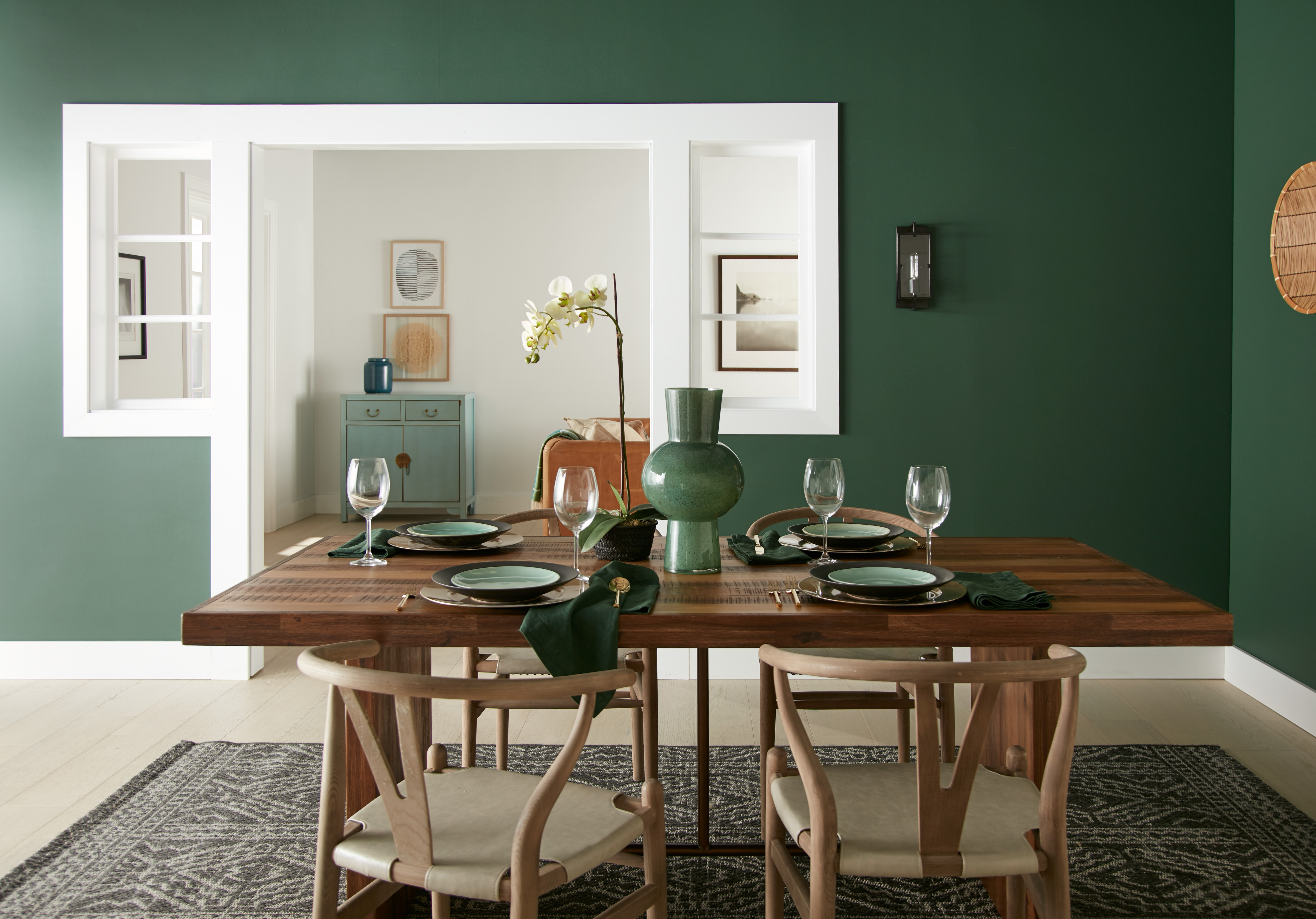 Une salle à manger avec des murs peints dans une couleur de vert profond et une table et chaises en bois clair et foncé au milieu.