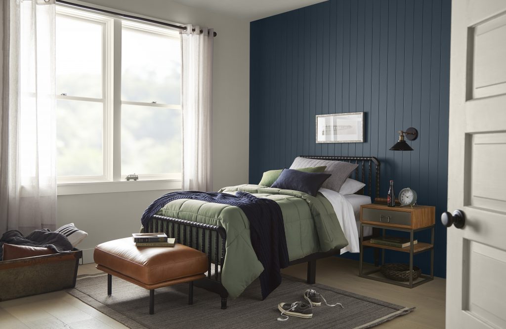 Une chambre à coucher charmante avec des murs peints en gris clair et un mur d'accent peint en bleu nuit, avec des verts profonds, bruns et blancs dans le décor et les meubles.