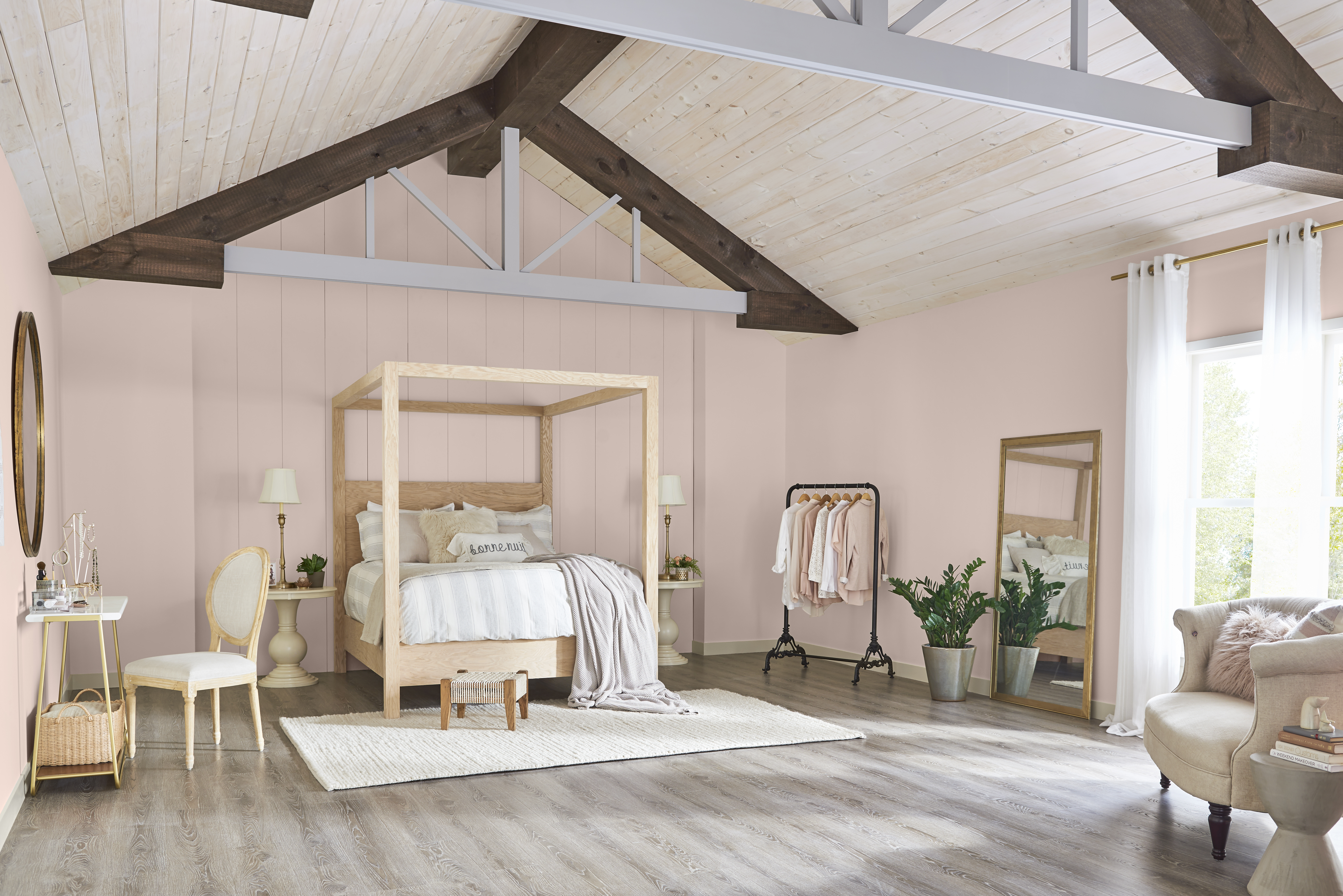 Une chambre aux murs peints en Rose fumé avec un grand lit à baldaquin en bois décoré de coussins et literie aux tons neutres