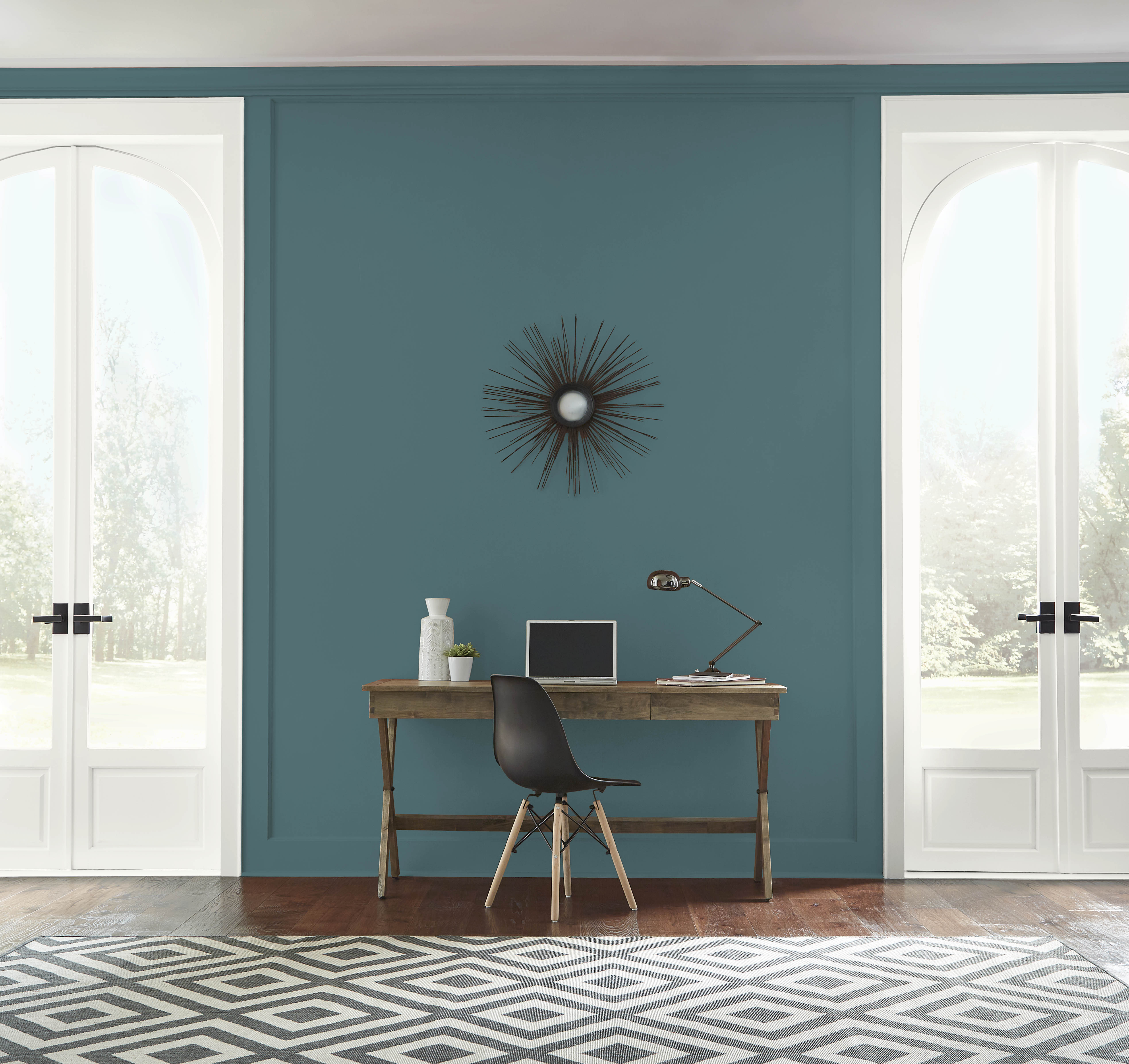 Un salon lumineux aux murs peints en Sarcelle sophistiquée, avec un pupitre et chaise en bois placés entre deux portes-fenêtres blanches