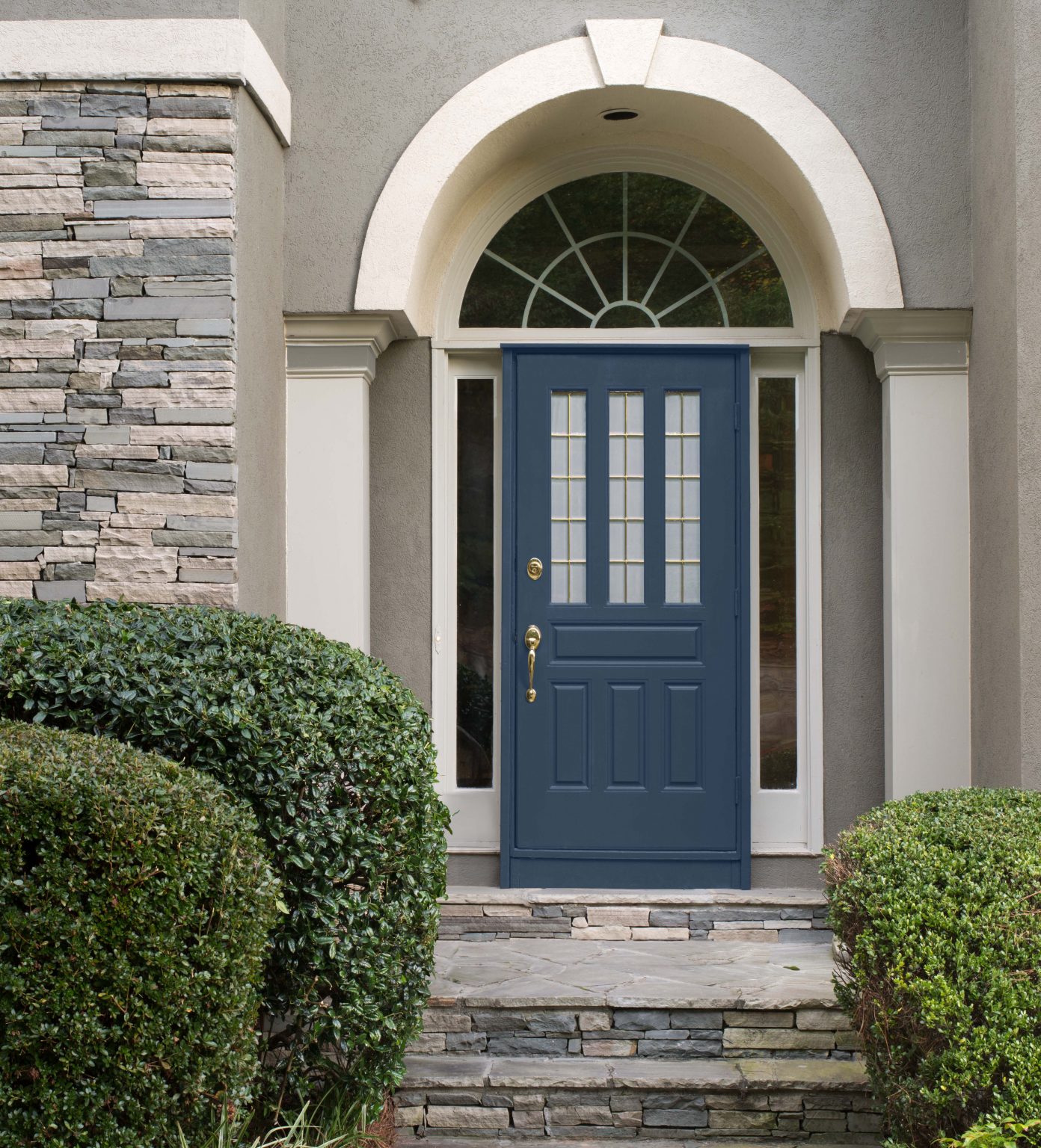 L'extérieur d'une maison avec brique et bardages en gris et porte d'entrée peinte en Bleu boussole