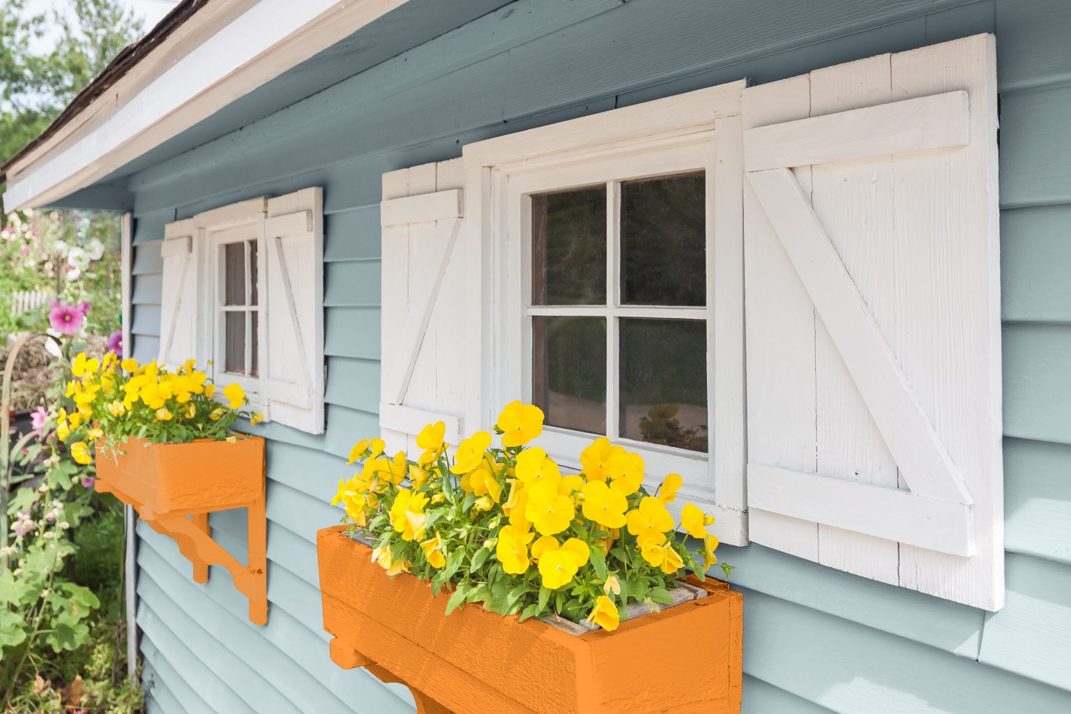 L'extérieur d'une maison avec deux jardinières dans la couleur Orange joviale remplies de fleurs jaunes