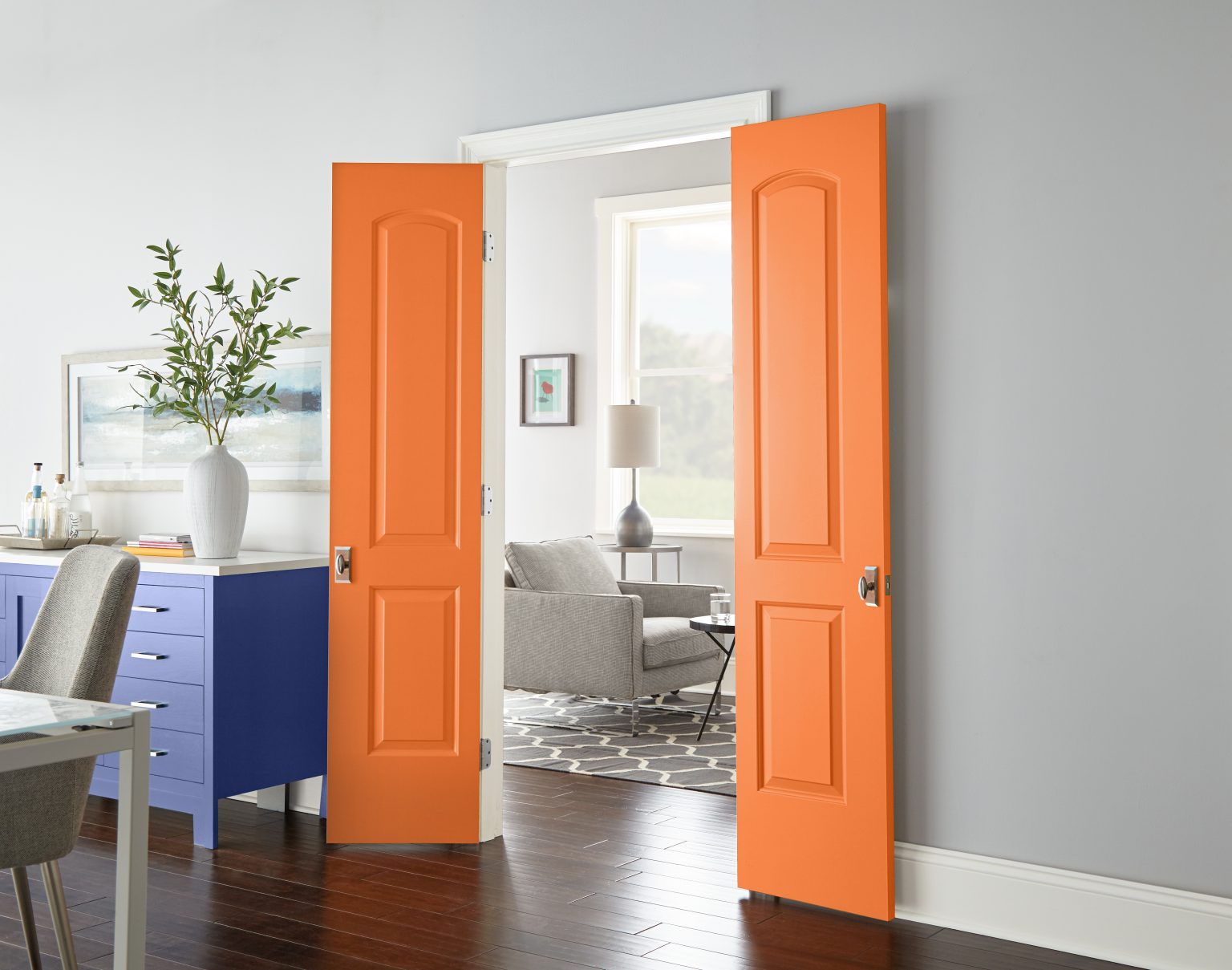 Une salle à manger avec une console dans la couleur Ciel lavande et des portes dans la couleur Orange acide ouvrant sur un salon