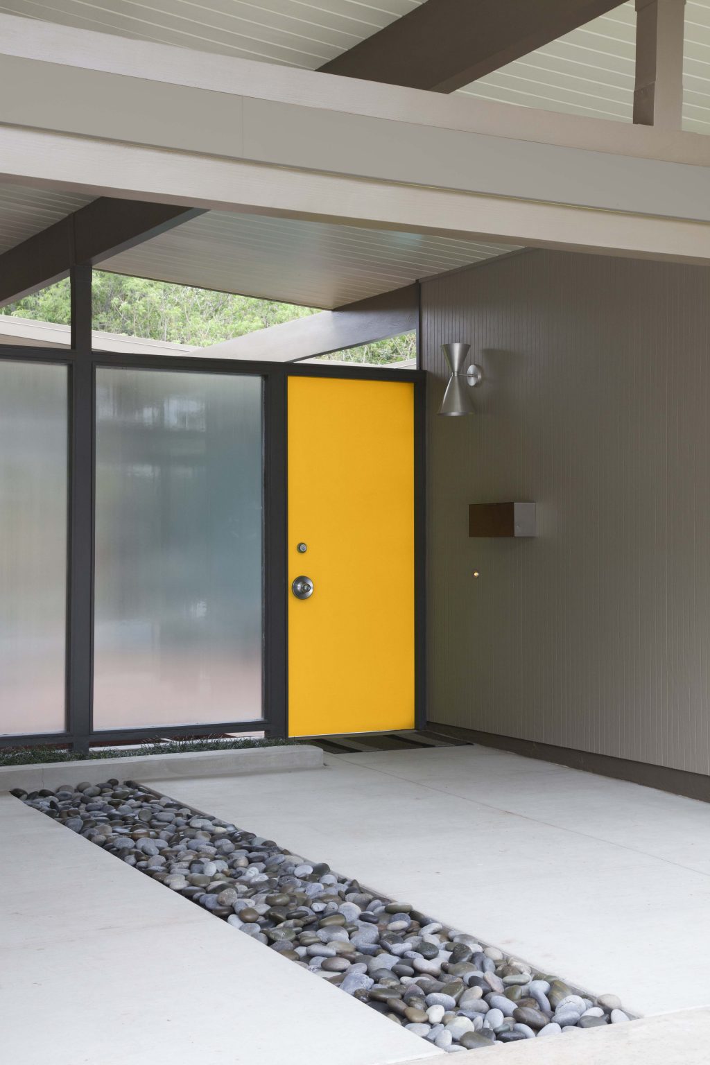 L'extérieur d'une maison moderne et minimaliste avec la porte d'entrée peinte dans la couleur Or milieu d’été