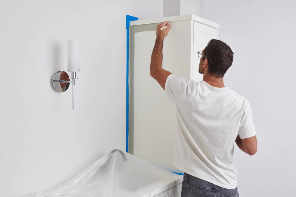 Un homme utilise un pinceau pour appliquer de la peinture sur les bords des armoires de la salle de bain