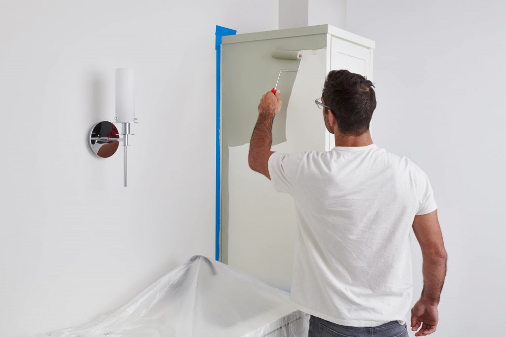Un homme utilise un petit rouleau pour appliquer de la peinture sur le corps des armoires de la salle de bain