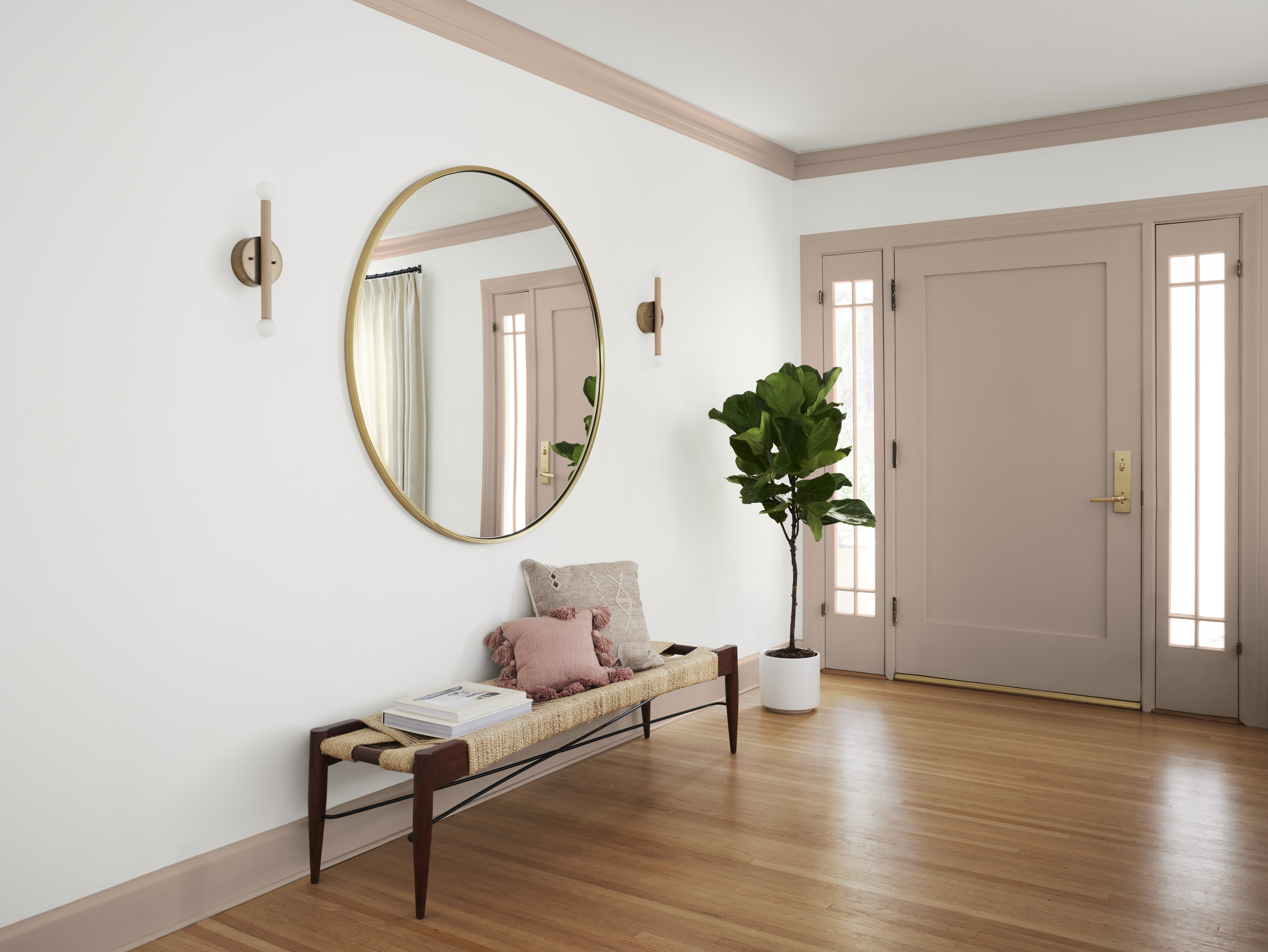 Une entrée spacieuse avec des murs en blanc et porte/garnitures en taupe, décorée d'un miroir rond, d'un banc et d'une plante