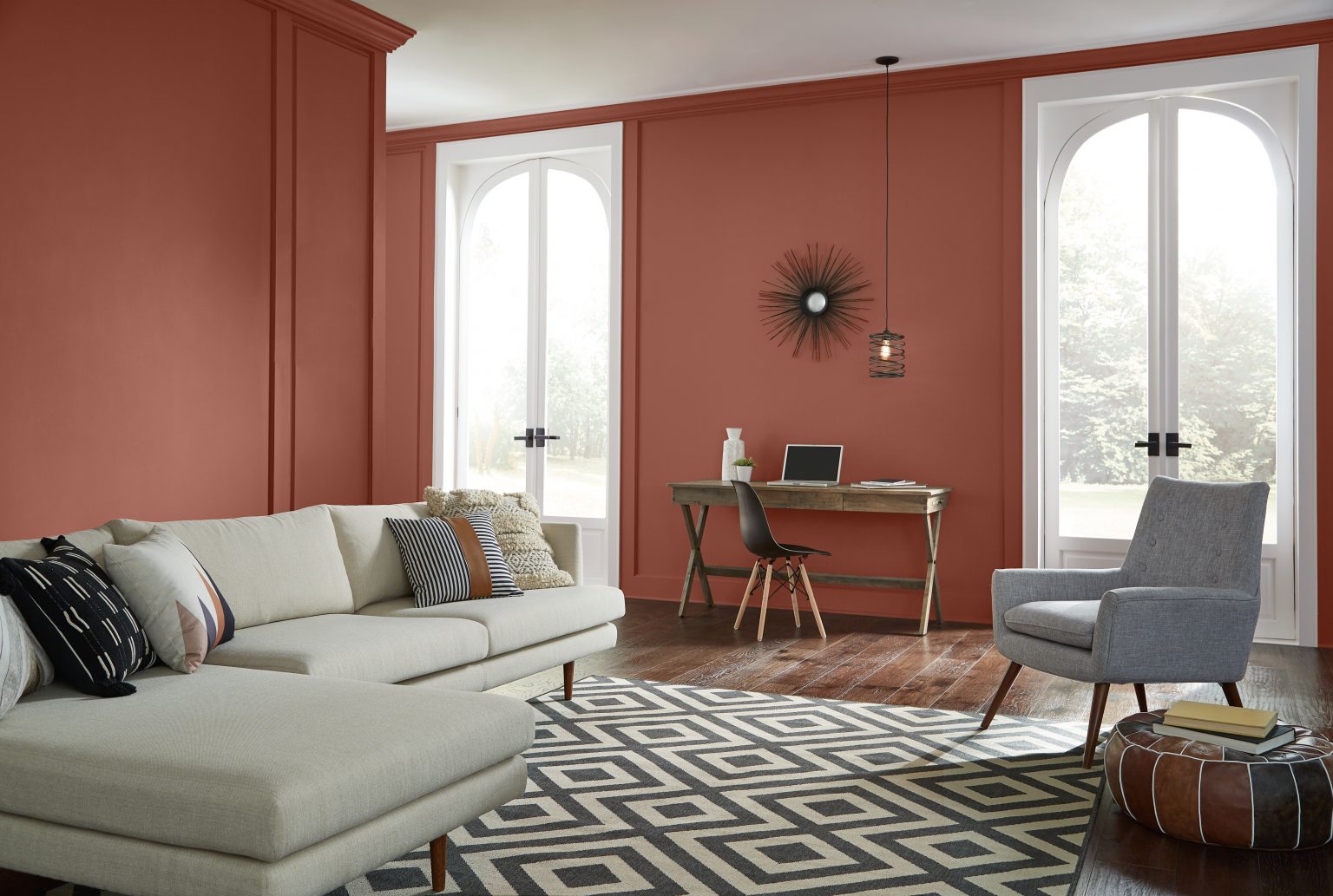 Un salon aux murs peints dans un rouge chaud, agrémenté d'un tapis géométrique et de meubles neutres
