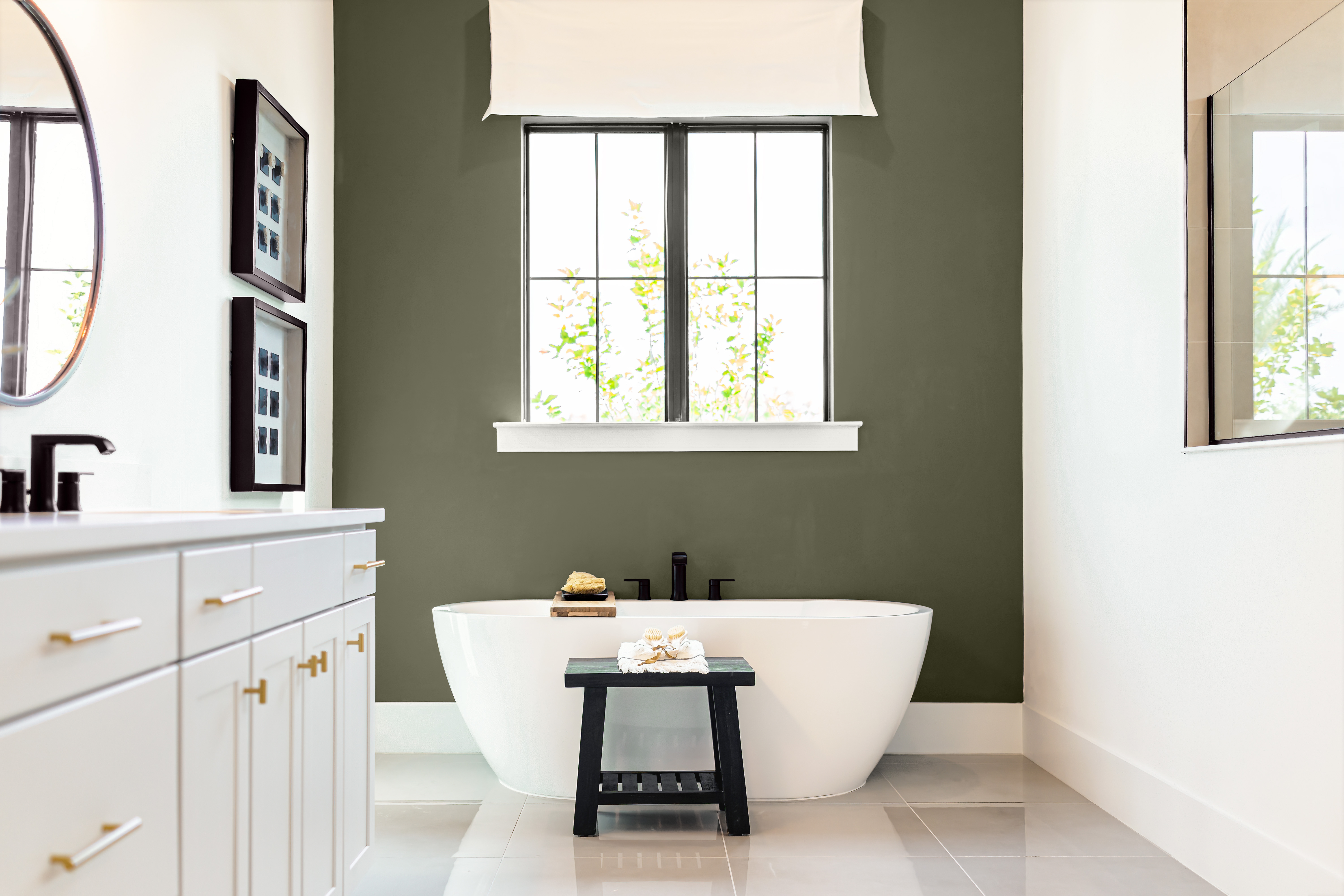 Une grande salle de bain avec deux murs peints en blanc et un mur d'accent peint en vert olive foncé, avec une baignoire blanche
