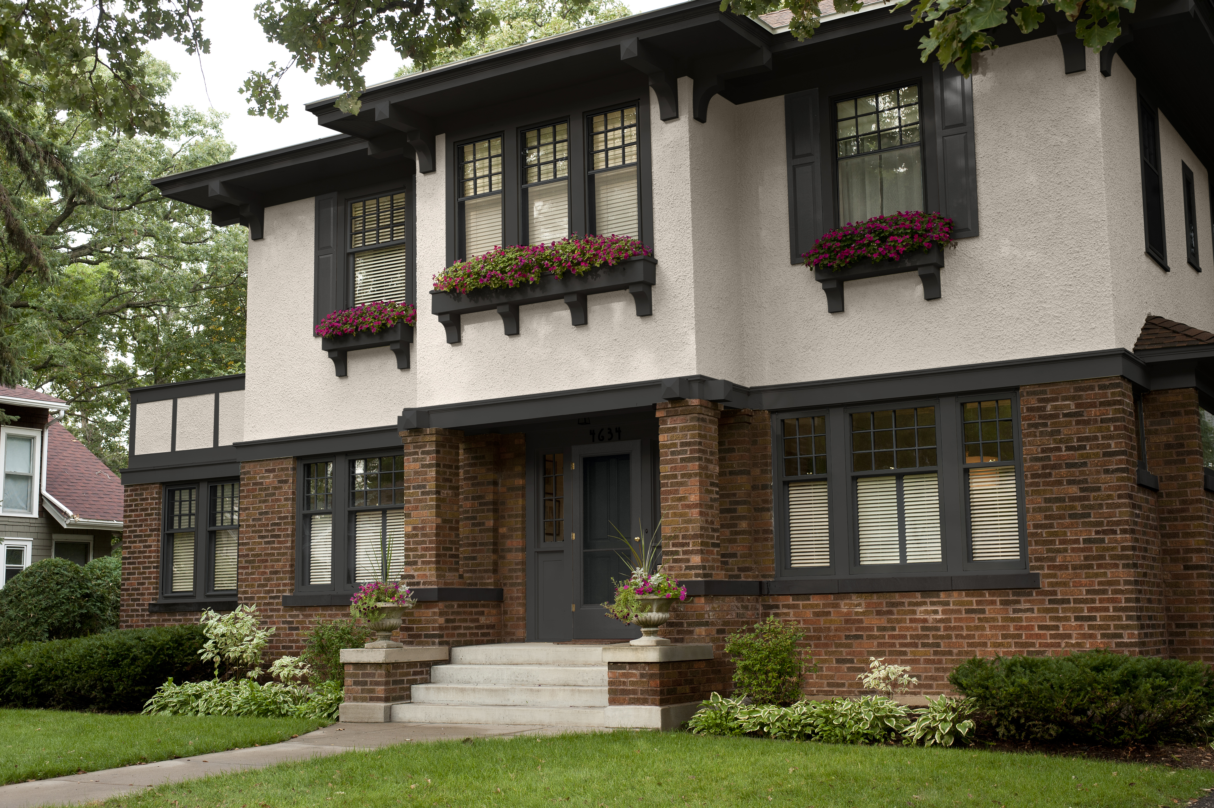L'extérieur d'une maison à deux étages avec du stuc beige, des briques rouges et brunes et des garnitures et accents noirs