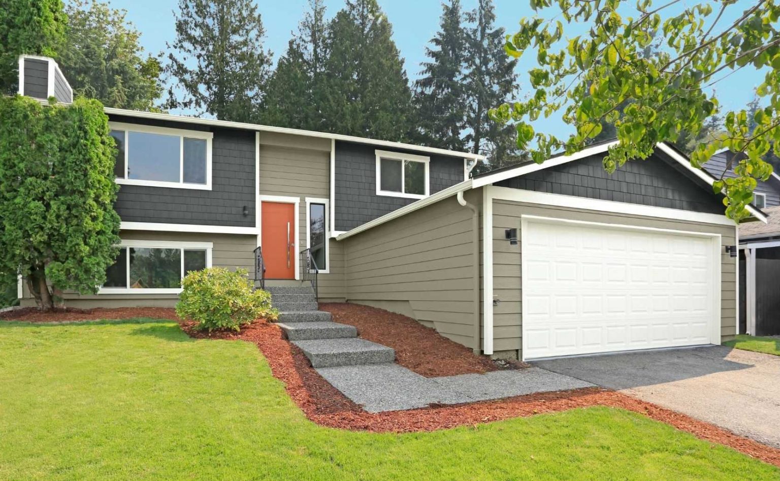 L'extérieur d'une maison à deux niveaux de style Ranch avec des planchettes en gris foncé et un revêtement vert terreux, ainsi qu'une porte en orange vif