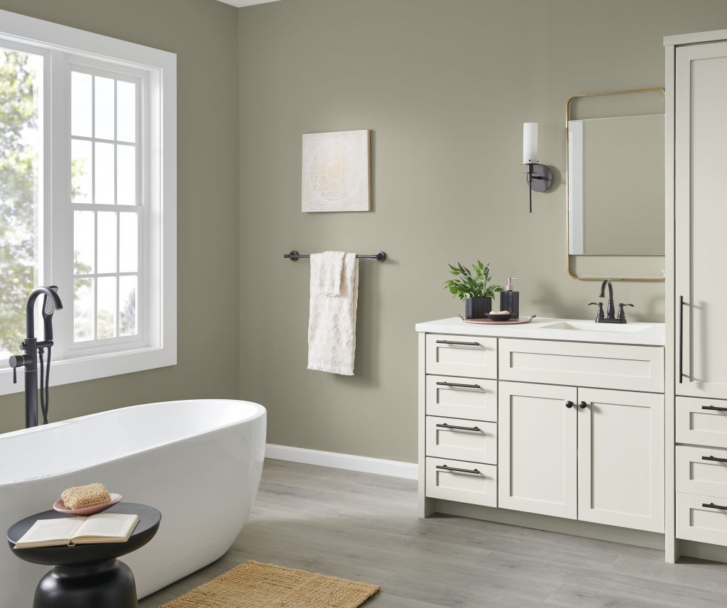 Une salle de bain spacieuse aux murs peints dans une couleur gris-vert aménagée d’une baignoire, d’un meuble-lavabo et d’armoires blanches