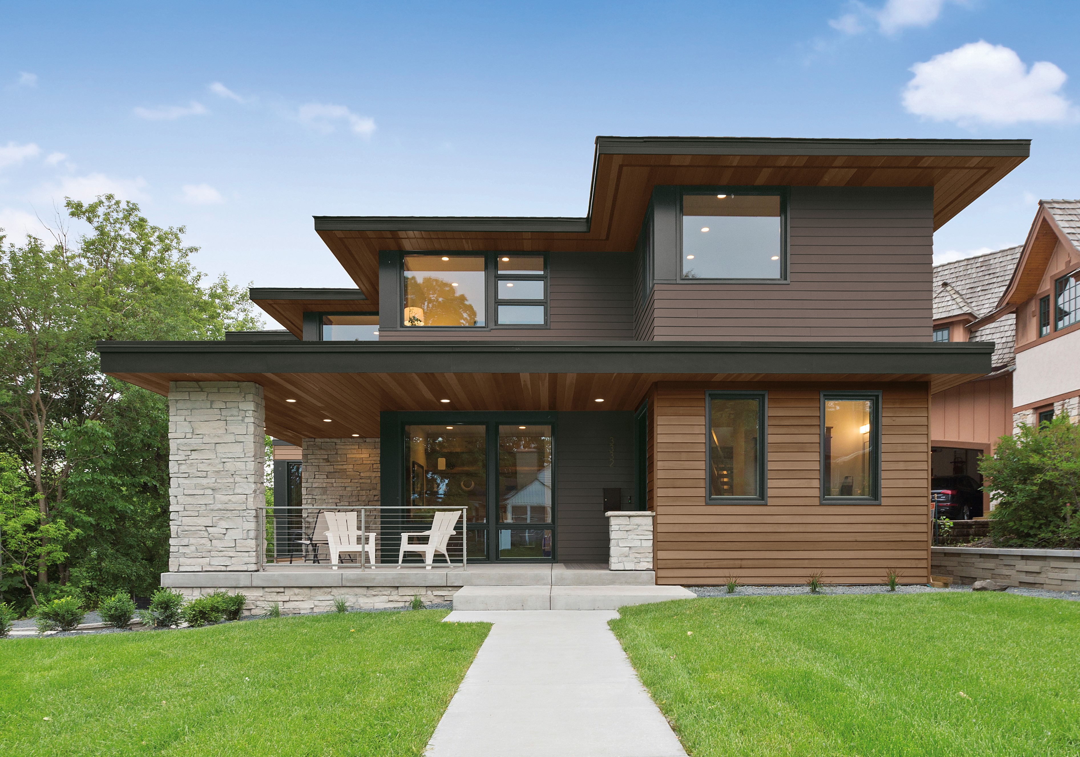 Une grande maison moderne à deux étages avec des bardages brun foncé et des garnitures noires dans la couleur Poivre concassé. La maison est dotée de bardages en bois qui ajoutent un élément naturel et sont complétés par une pelouse verte magnifiquement entretenue.