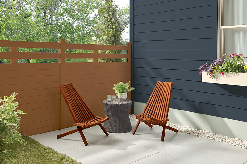 Un joli patio extérieur avec une clôture en bois teinte en Cèdre et une maison peinturée avec Bleu minuit, créant une atmosphère chaleureuse et tranquille.