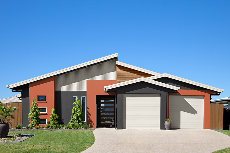 Une maison moderne avec une palette de couleurs amusantes composée de blanc, d'orange rouille et de noir doux. L'extérieur est complété par une petite clôture en bois qui ajoute de la chaleur et une touche naturelle à l’ensemble. 