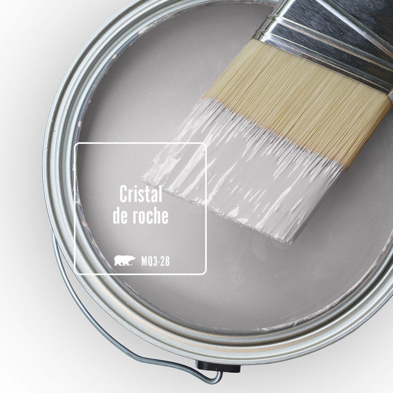 Vue du dessus d’un pot de peinture ouvert. La peinture est de couleur Cristal de roche, un gris clair nuancé de notes de lilas. Un pinceau à moitié trempé est posé sur le bord du pot.