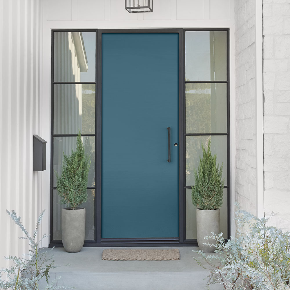 Cette image montre le porche d’entrée d’une ferme moderne avec un extérieur gris-violet clair, une porte bleue et des garnitures gris anthracite foncé, mêlant des couleurs contemporaines au charme classique de la ferme.