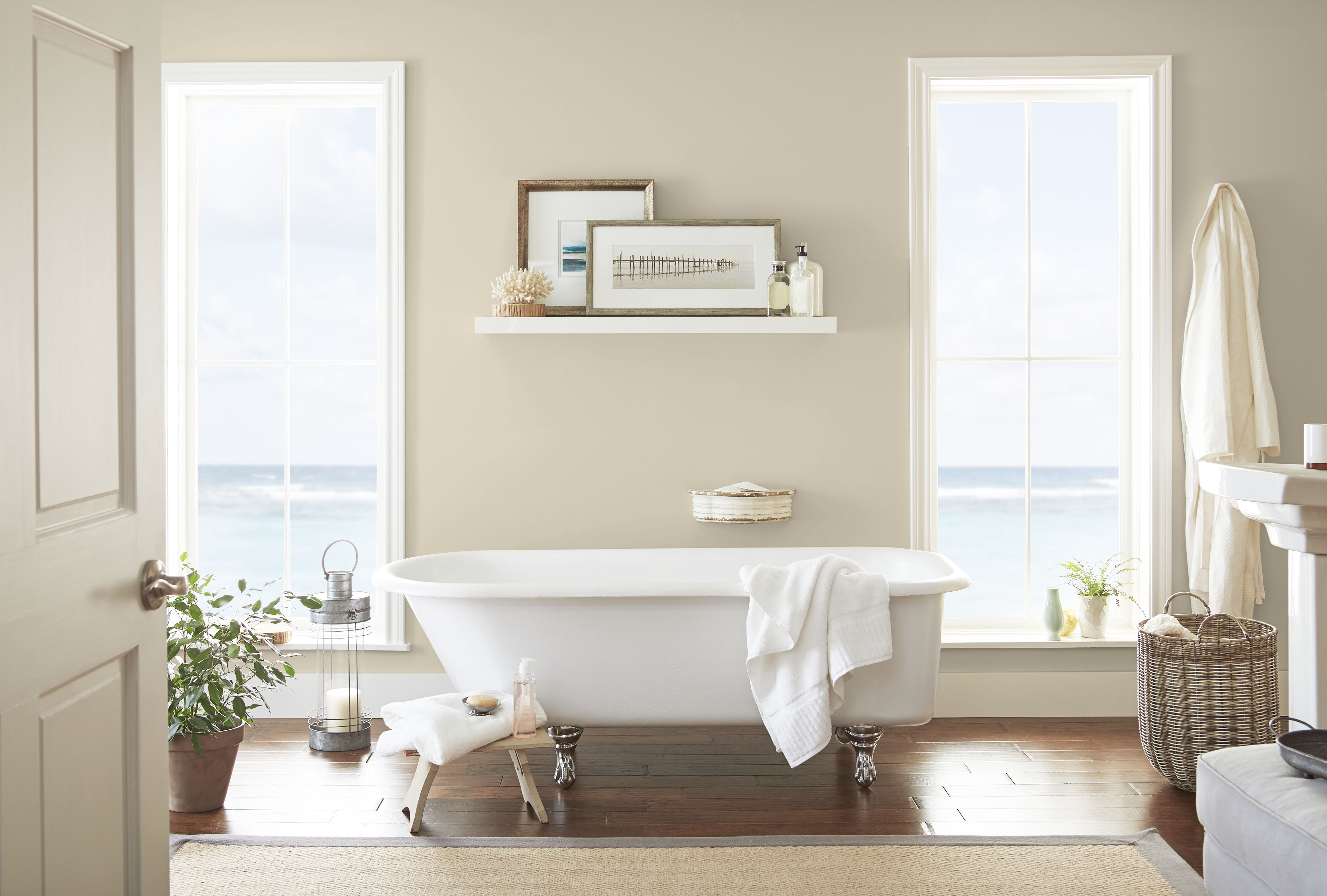 Cette image montre une salle de bain avec deux grandes fenêtres donnant sur l’océan et des murs peints dans une douce nuance de beige.