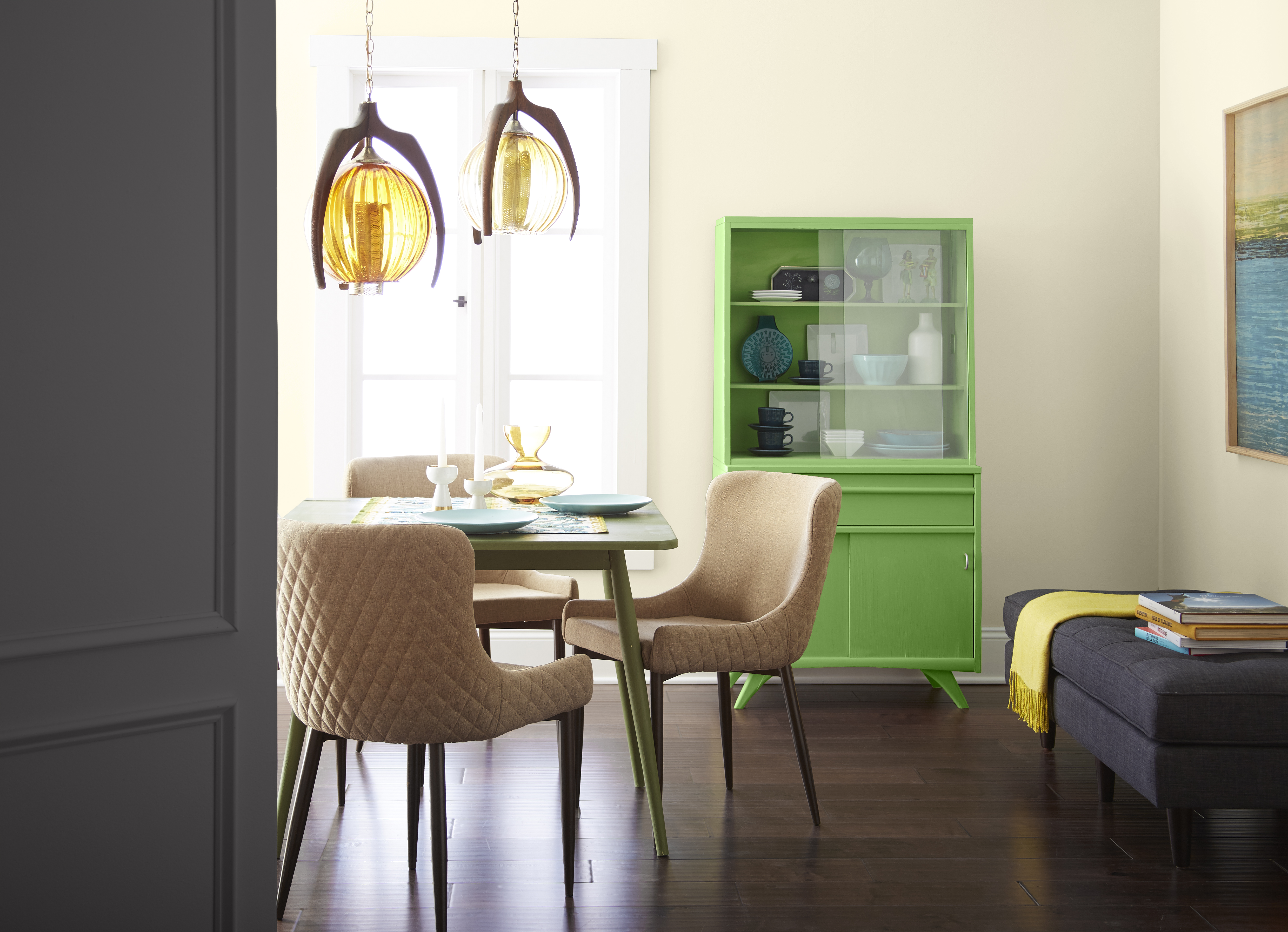 Cette image montre une petite salle à manger avec un mur jaune très pâle et un vaisselier de couleur vert vif.