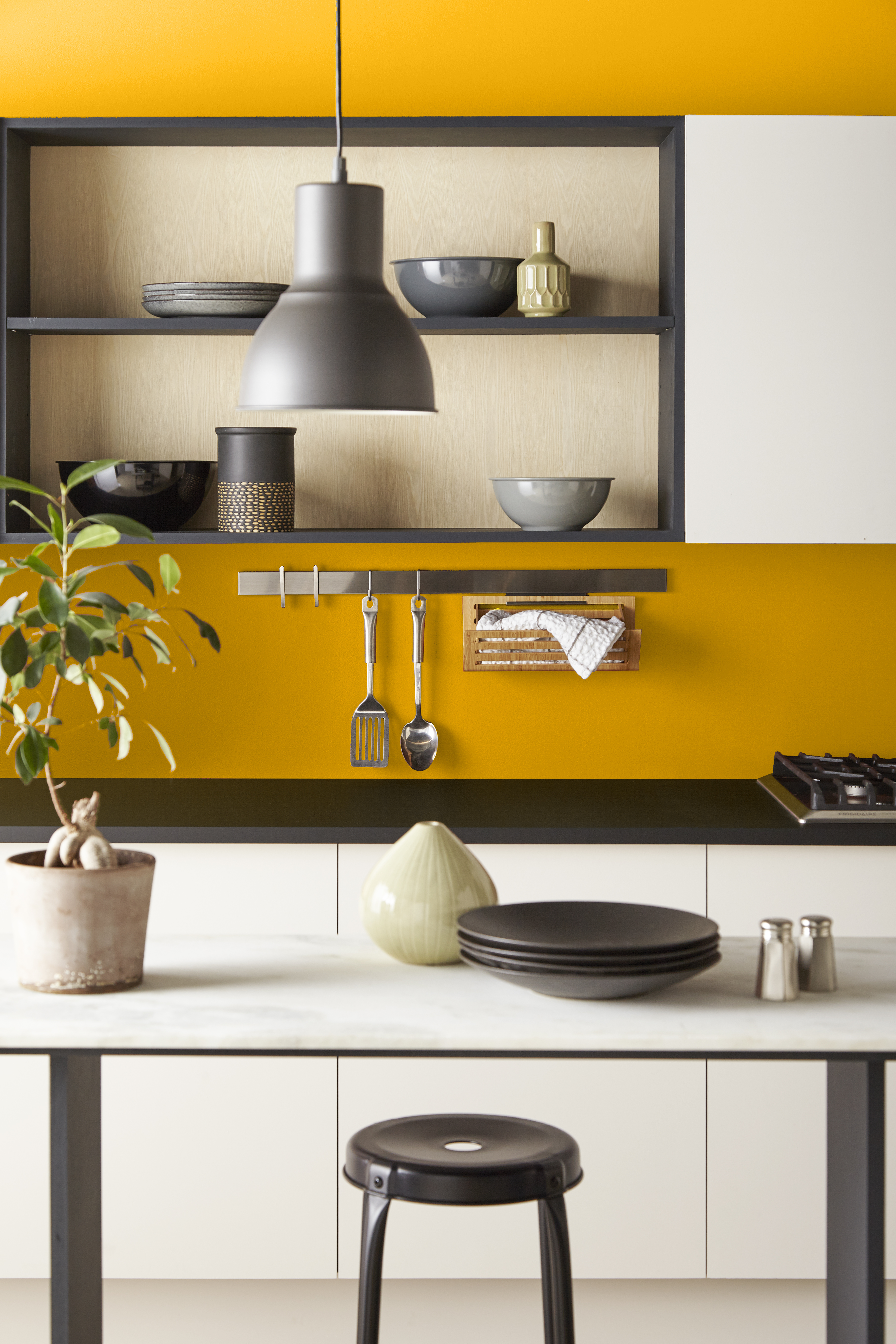 Cette image montre une cuisine avec un mur jaune foncé et des armoires blanc crème.
