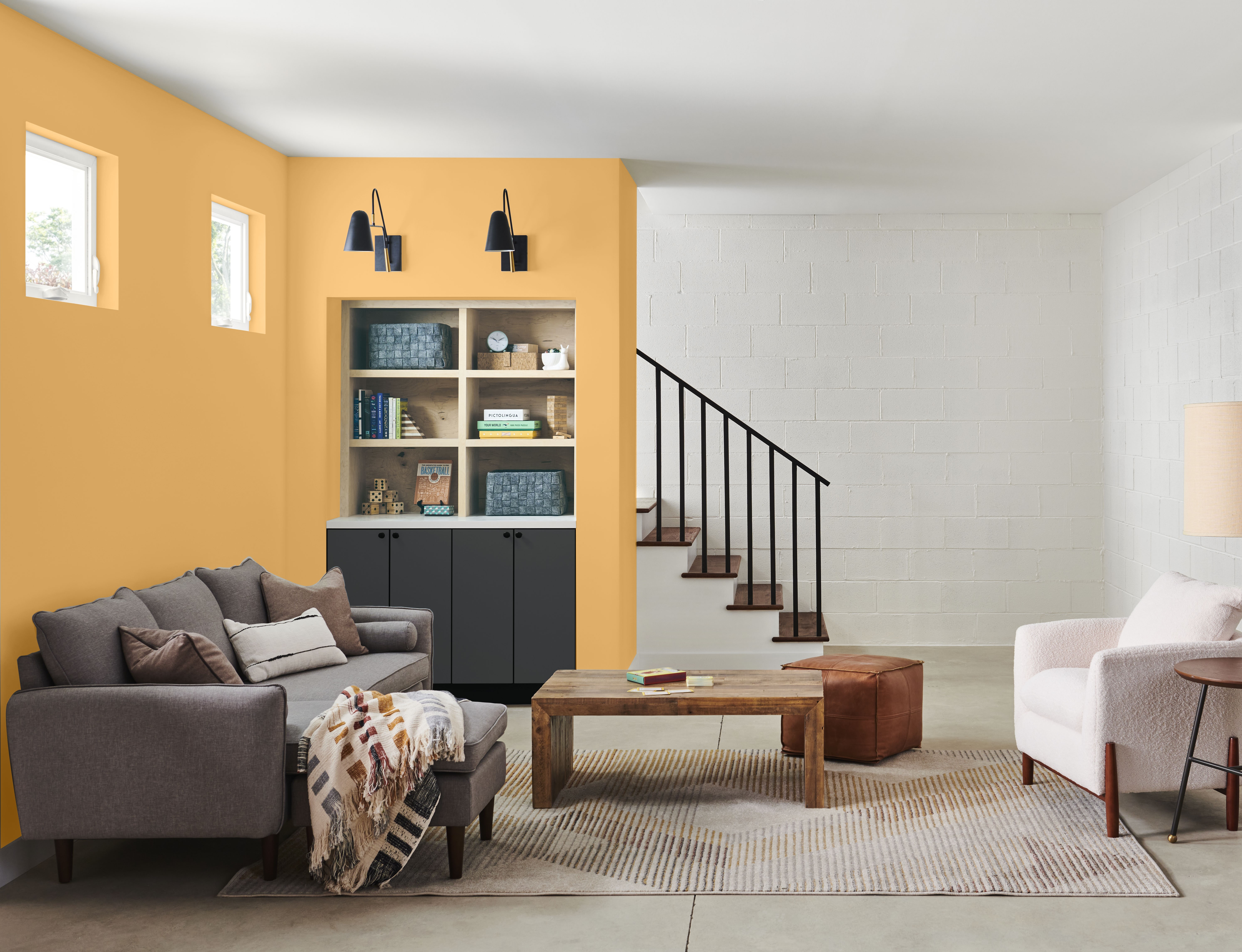 Cette image montre un espace de vie au sous-sol, où se trouvent un sofa confortable, un mur d’accent en L peint en jaune vif, ainsi qu’une unité murale dont les armoires du bas sont peintes d’un noir doux, ce qui confère à l’espace une ambiance à la fois douillette et moderne grâce au contraste marqué des couleurs.