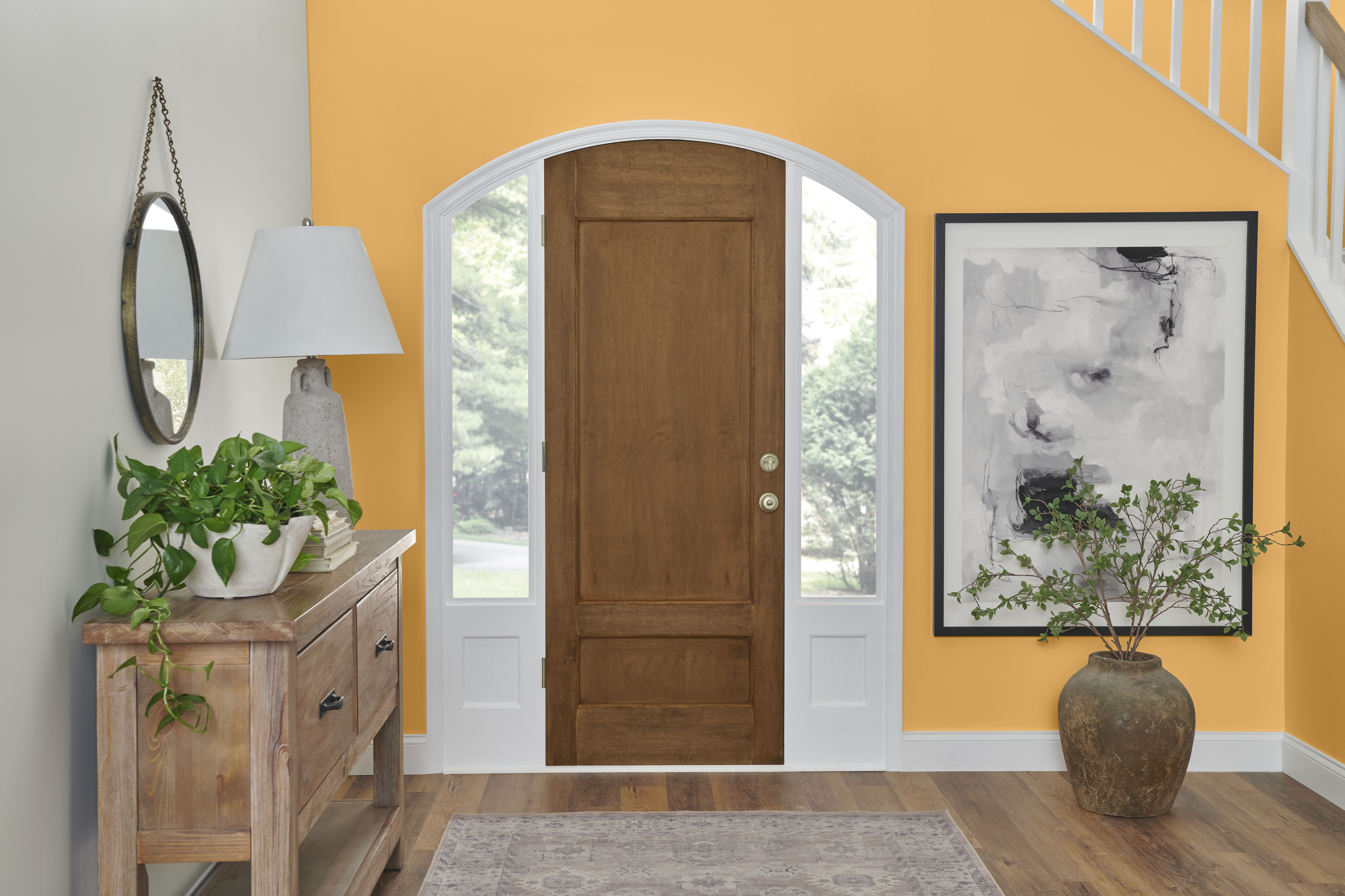 Cette image montre un hall d’entrée avec une porte de bois et des murs blancs. Deux murs peints en jaune Jacquier servent à accentuer l’espace, ajoutant une touche de couleur éclatante et accueillante qui contraste avec la neutralité des autres couleurs.