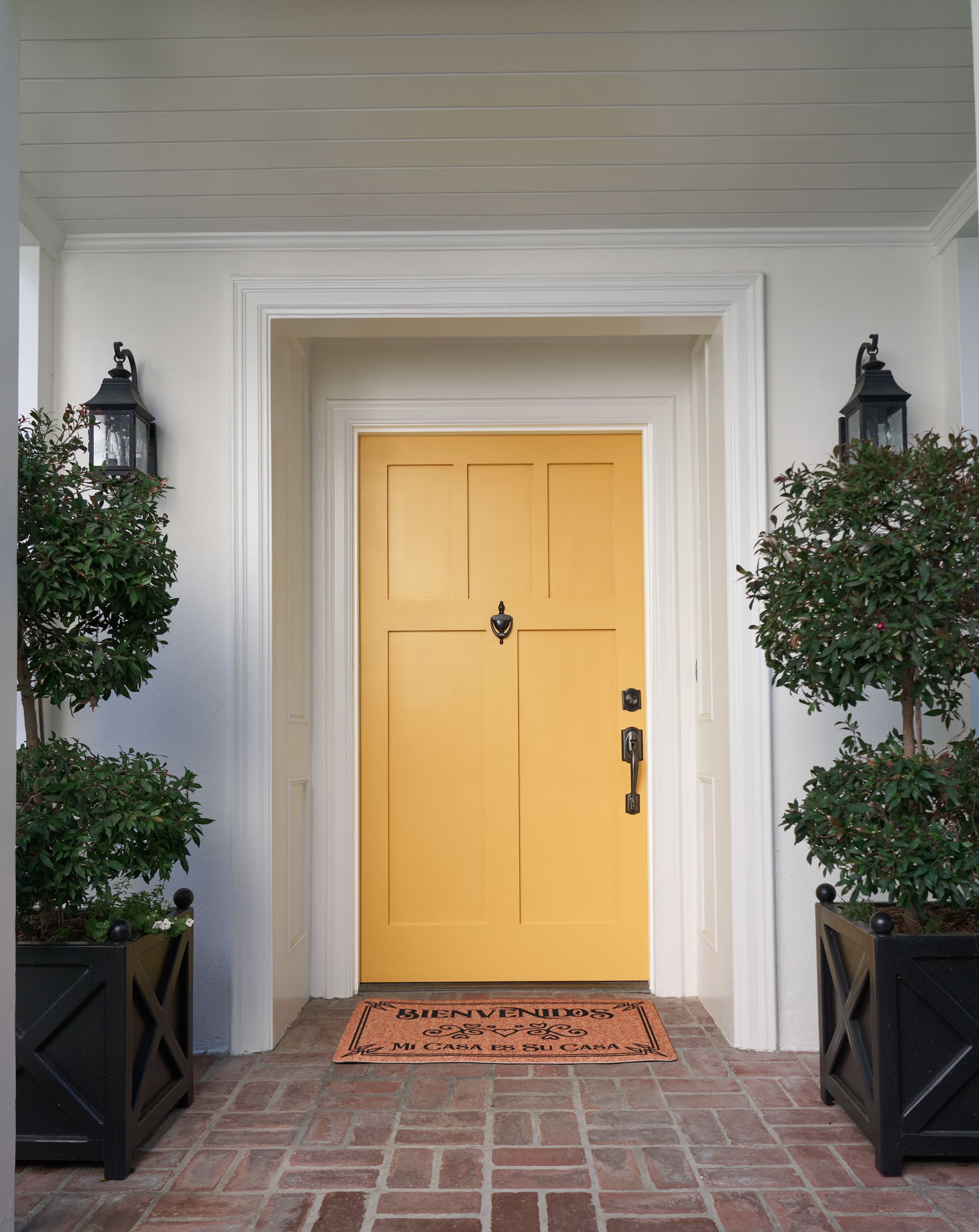 Cette image montre l’entrée principale d’une maison de couleur blanche avec une porte jaune vif, créant ainsi un point focal audacieux et accueillant contre l’extérieur neutre et épuré.