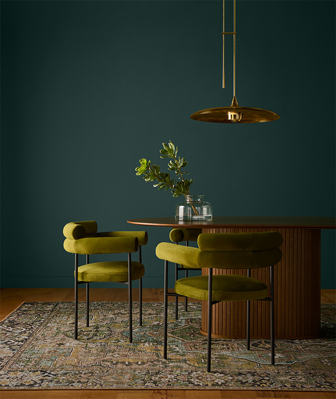Cette image montre une salle à manger d’un chic contemporain, avec une table ovale en bois et deux chaises en velours rétro-modernes. Le mur est peint en Bijou caché, un jade fumé qui distille l’élégance avec un air de sophistication.