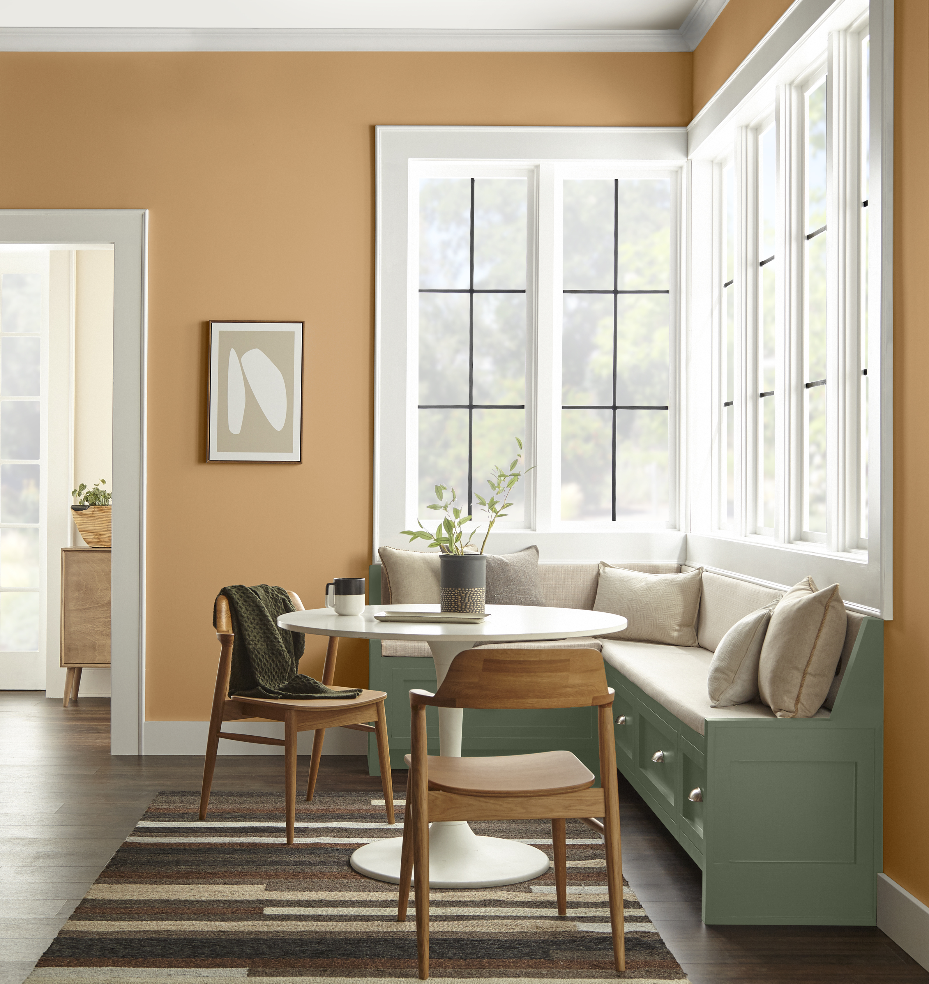 Cette image montre un coin-repas avec des murs peints en caramel orangé et une banquette peinte en un vert profond.