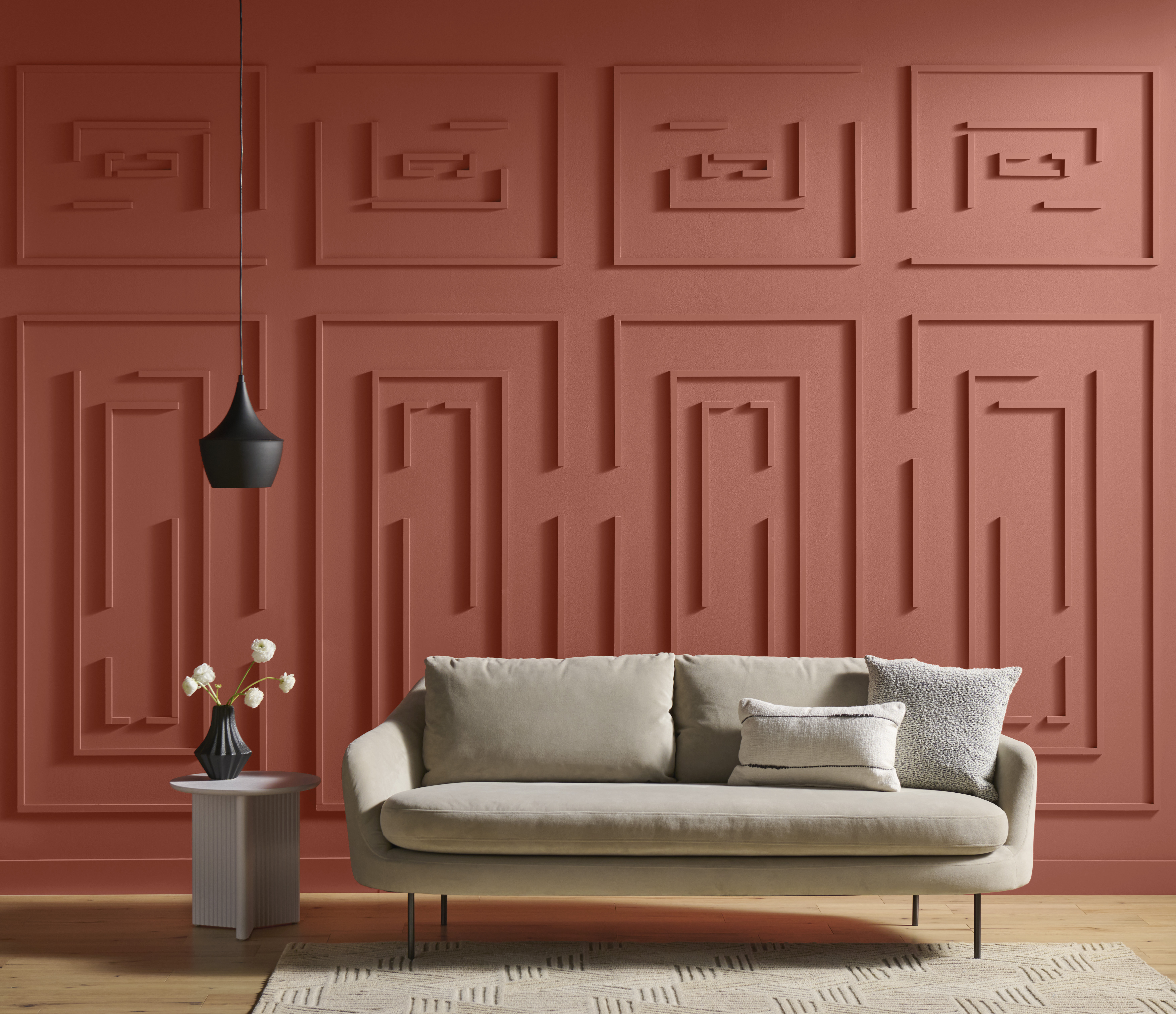 Cette image montre un divan de couleur neutre dans une pièce dont le mur est orné de panneaux décoratifs en forme de labyrinthe.