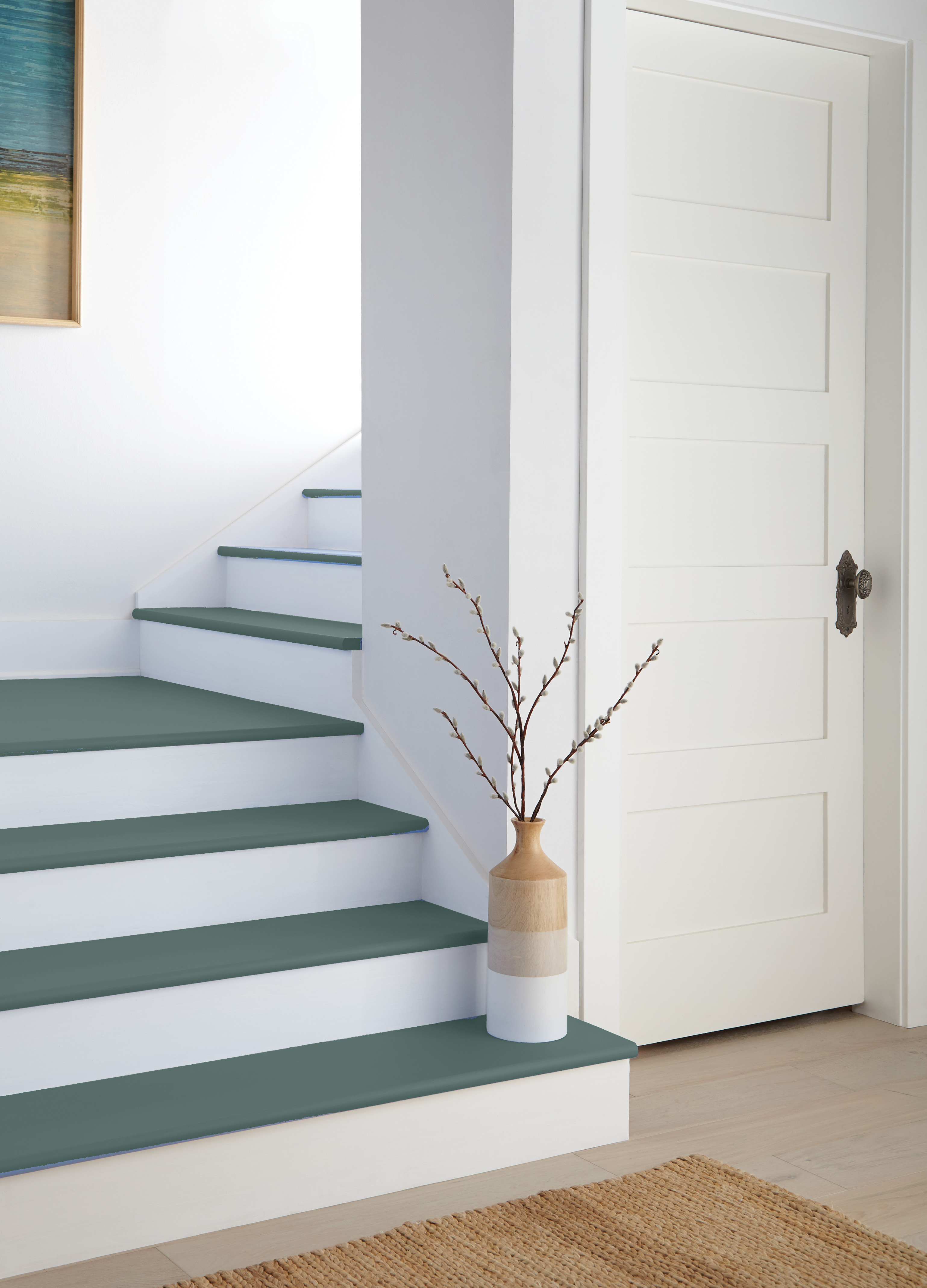 Cette image montre un escalier intérieur moderne, avec des contremarches blanches et des marches bleu sarcelle, qui contourne une porte à panneaux et au pied duquel on voit un tapis tissé.
