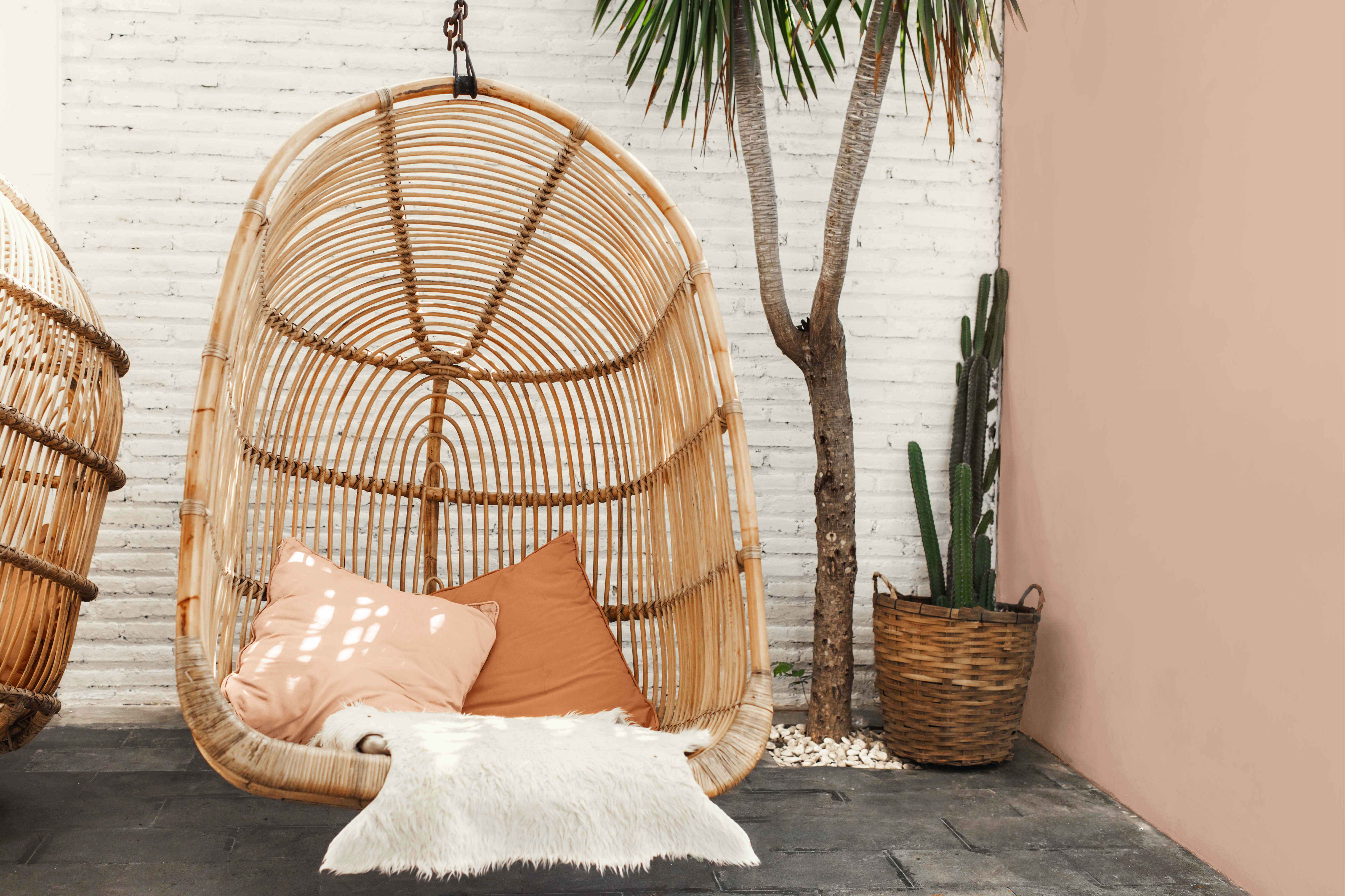Alt text: Cette image montre une grande chaise suspendue en bambou naturel à côté d’un mur dont le crépi est peint en un ton de terre cuite pâle.